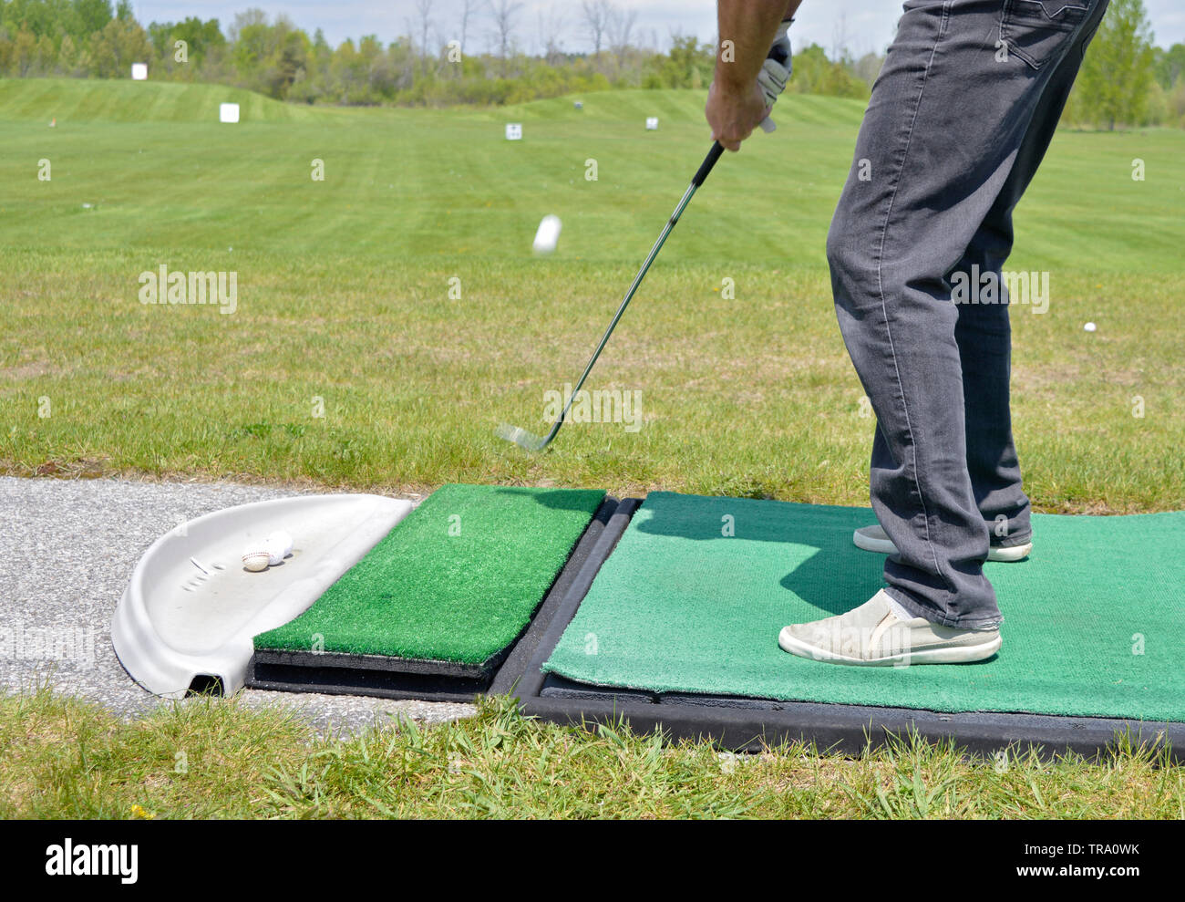Golfer takes a practice shot at the driving range. Ball and club in