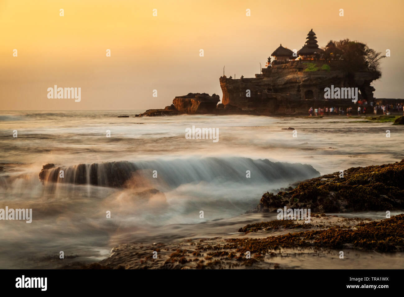 Tanah Lot Temple sunset view from a distance with a long exposure creative photography effect used to capture the incoming tide and breaking waves Stock Photo