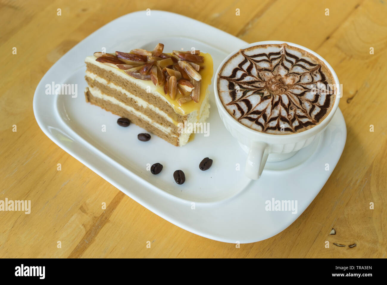 hot coffee late in white glass on wooden table, blurred cake and wooden spoon, Stock Photo