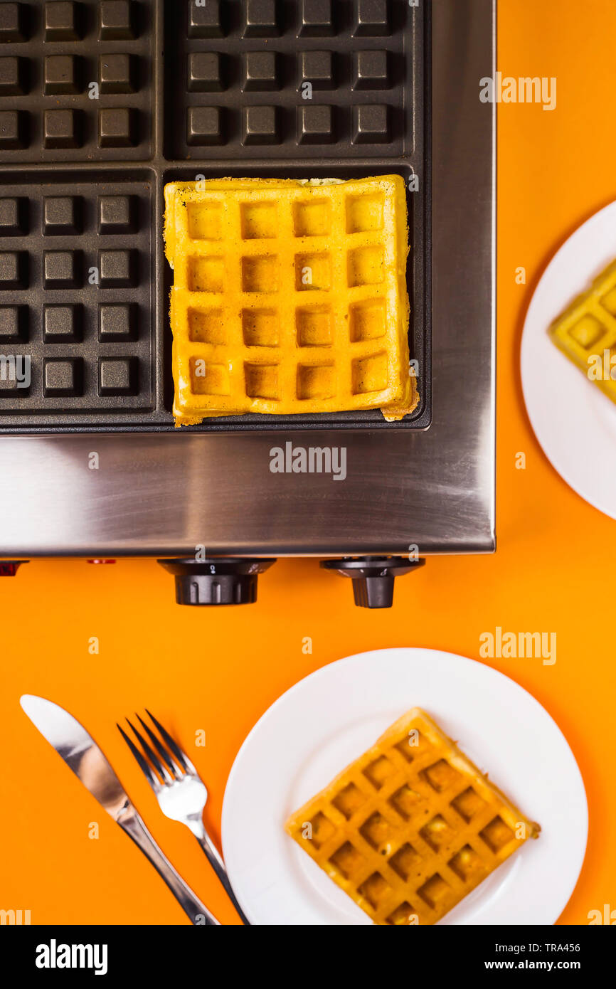 Waffle iron and ready made belgian waffles on plates on a bright yellow