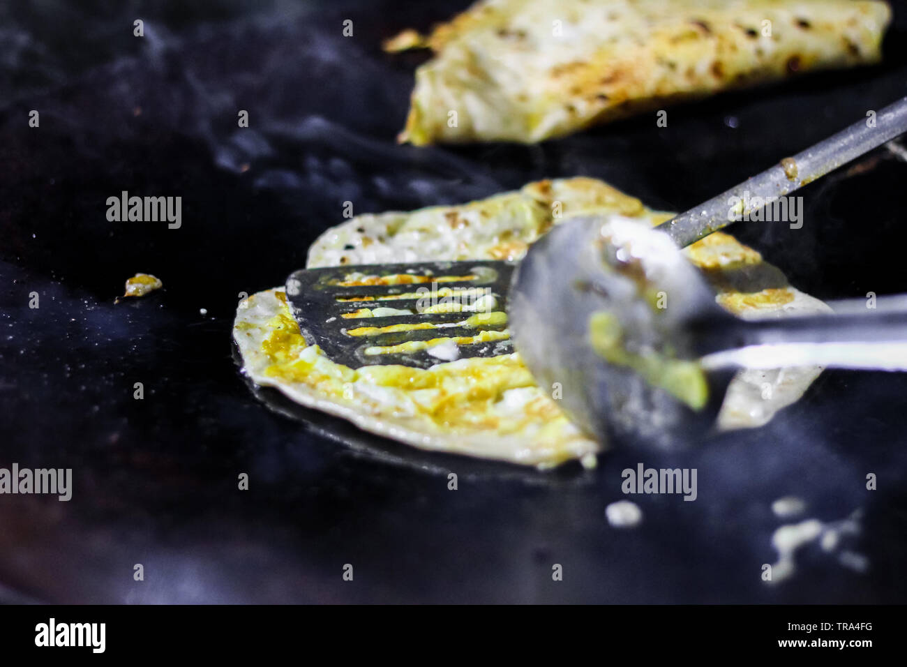making of egg roll on a hot frying pan with oil and paratha and salad