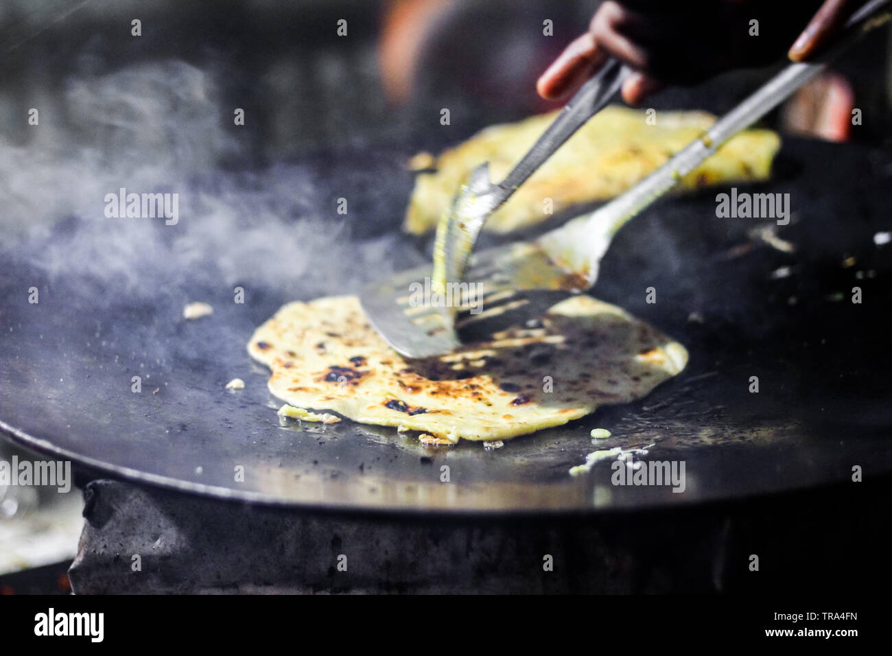 making of egg roll on a hot frying pan with oil and paratha and salad
