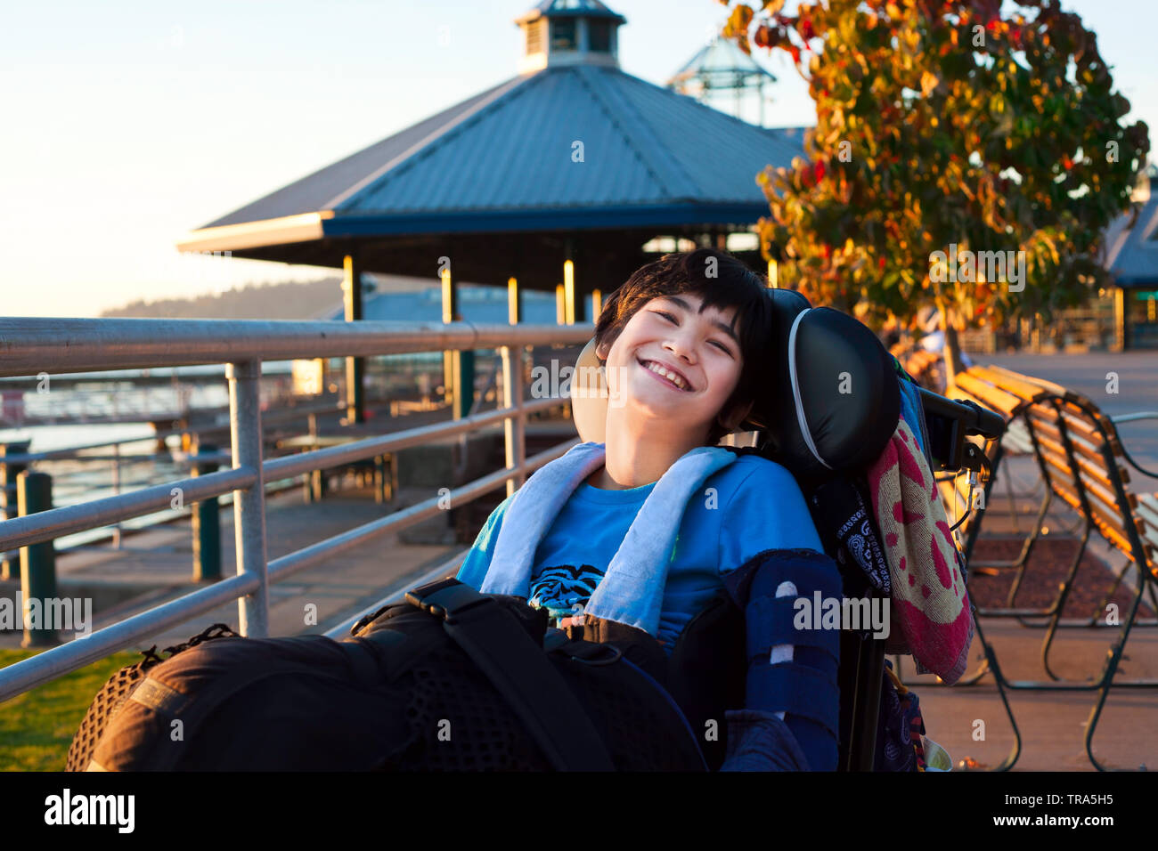 Happy smiling little twelve year old disabled boy in wheelchair outdoors enjoying summer evening at park Stock Photo