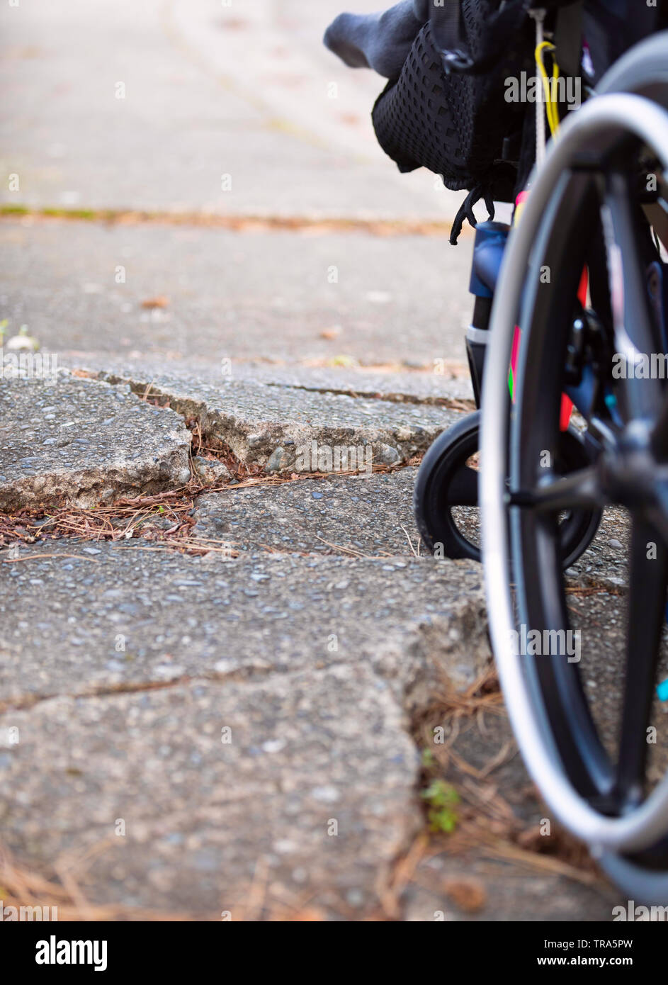 Wheelchair wheel stuck against large cracks in broken sidewalk pavement