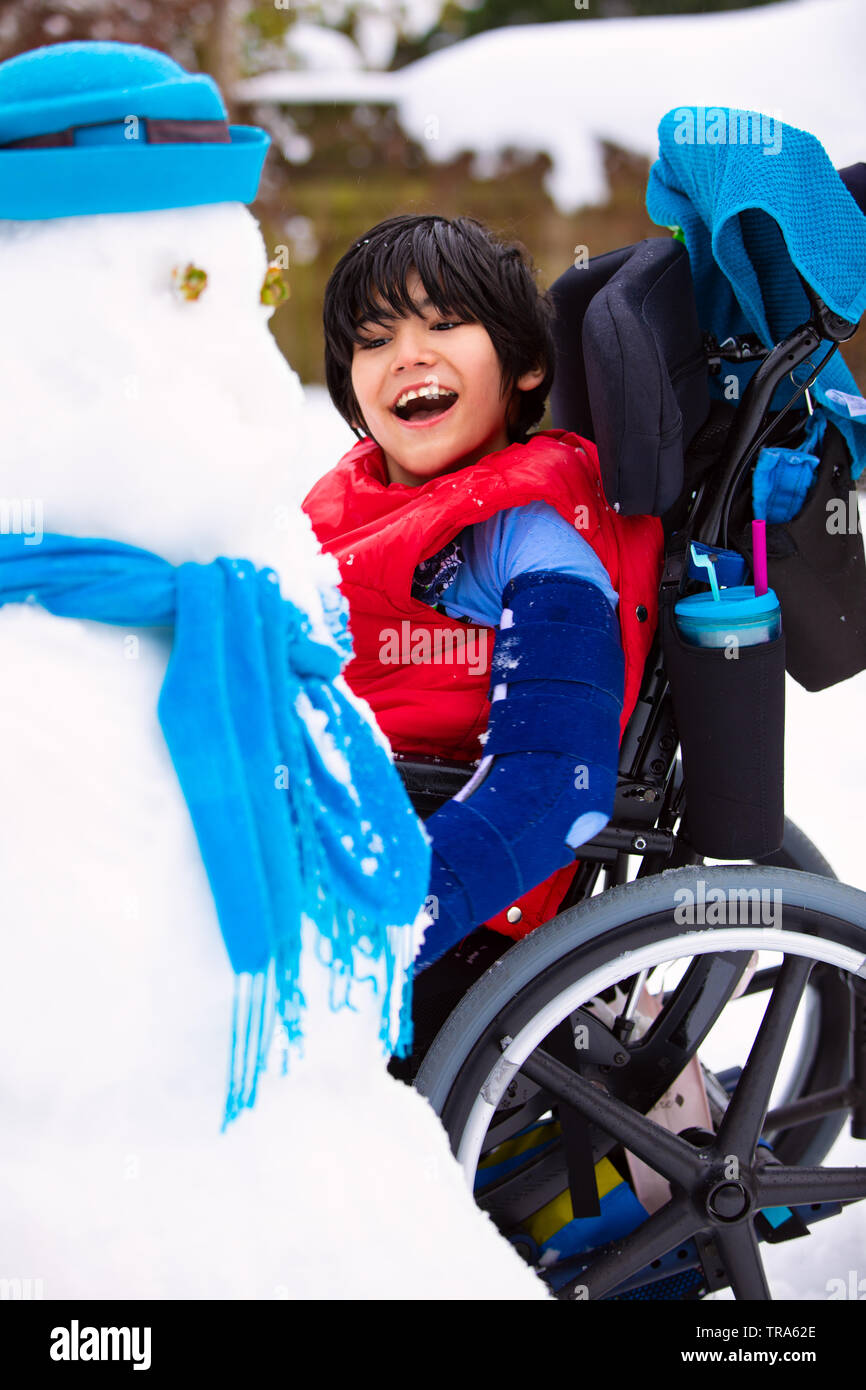 Happy smiling disabled boy in wheelchair building a snowman Stock Photo