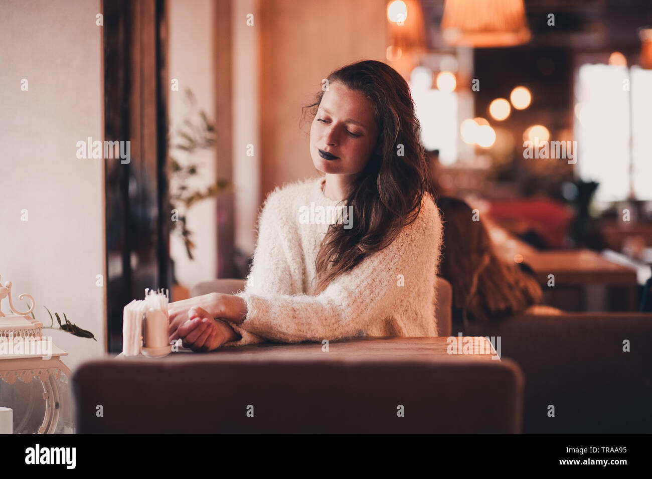 Stylish girl 24-29 year old sitting in restaurant wearing fluffy white sweater. 20s. Stock Photo