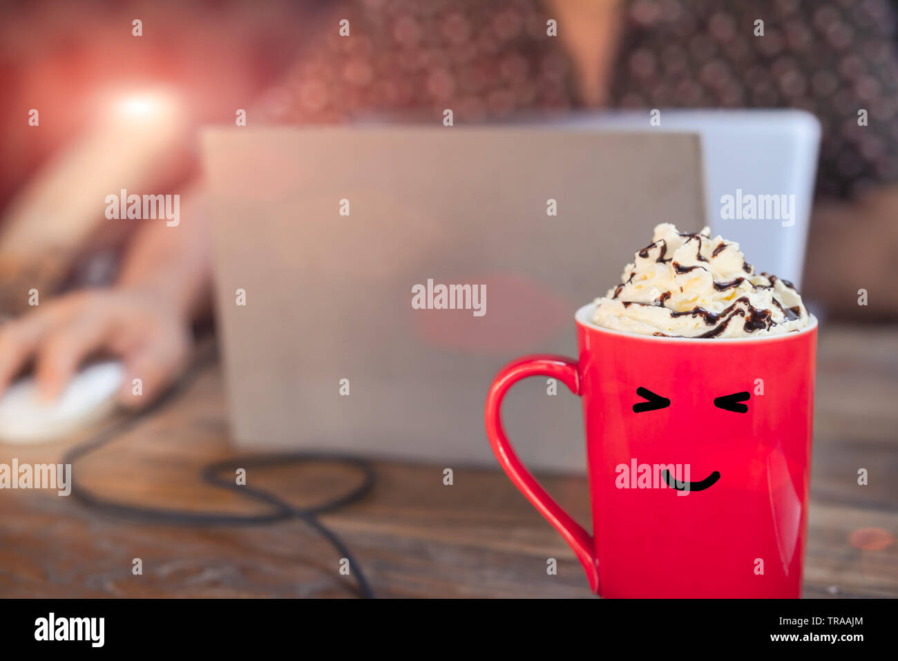hot mocha coffee in red cup with smile face on wooden table with working man using laptop Stock Photo