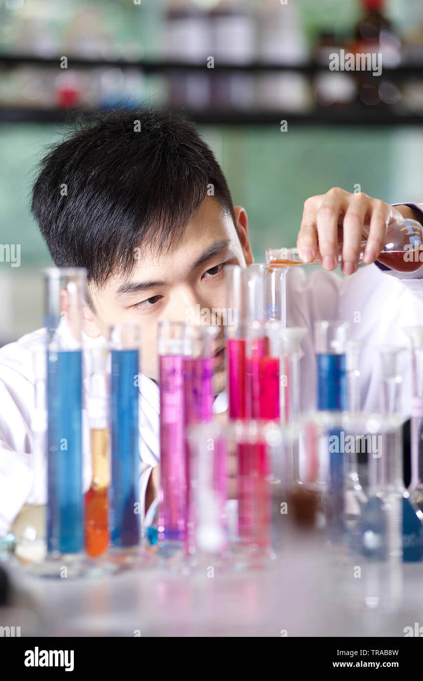 Young Asian professor focussed doing tests in a laboratory using a