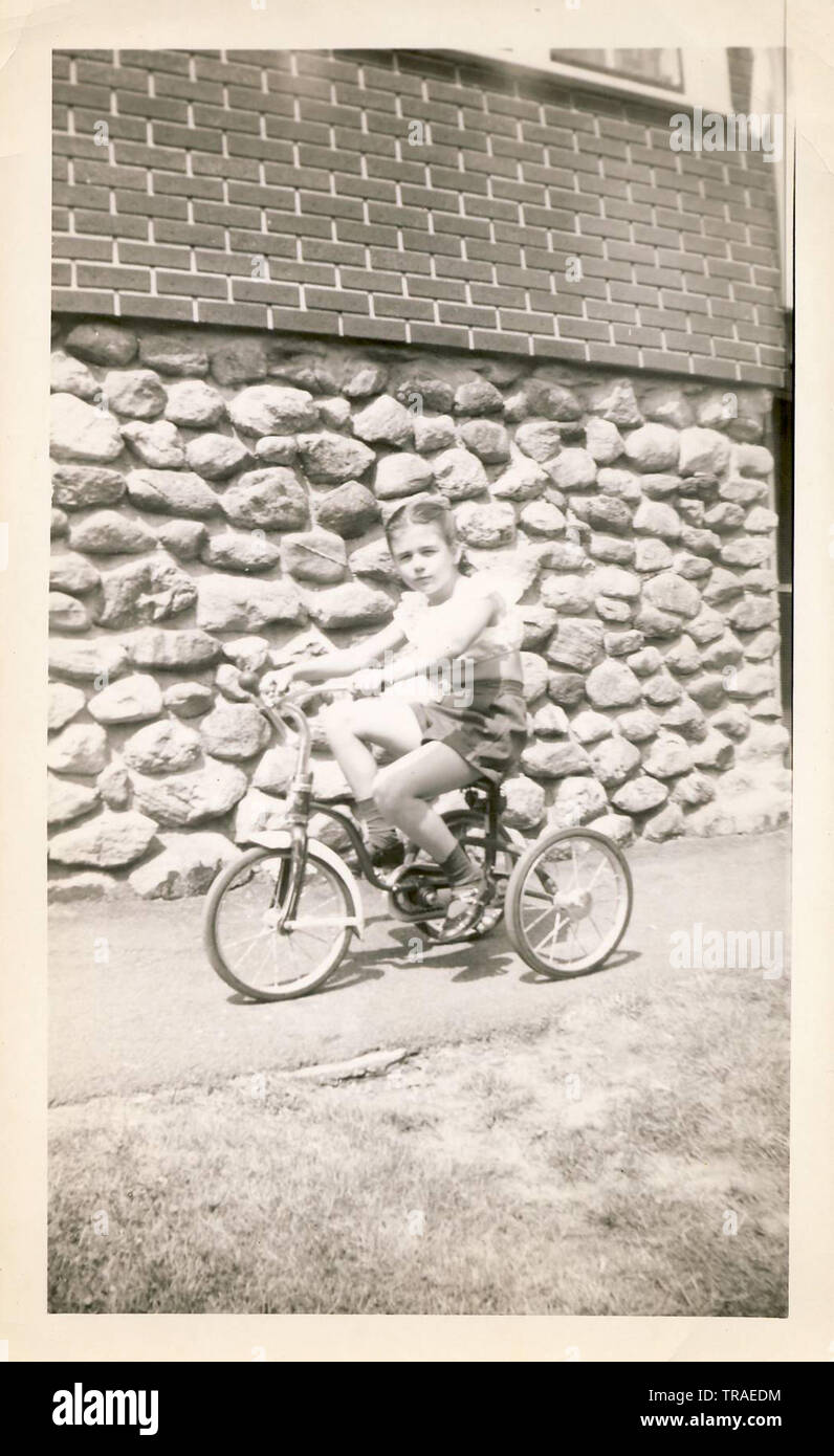 A vintage black and white photo of a young girl riding a bicycle, circa late 1940s, early 1950s. Stock Photo