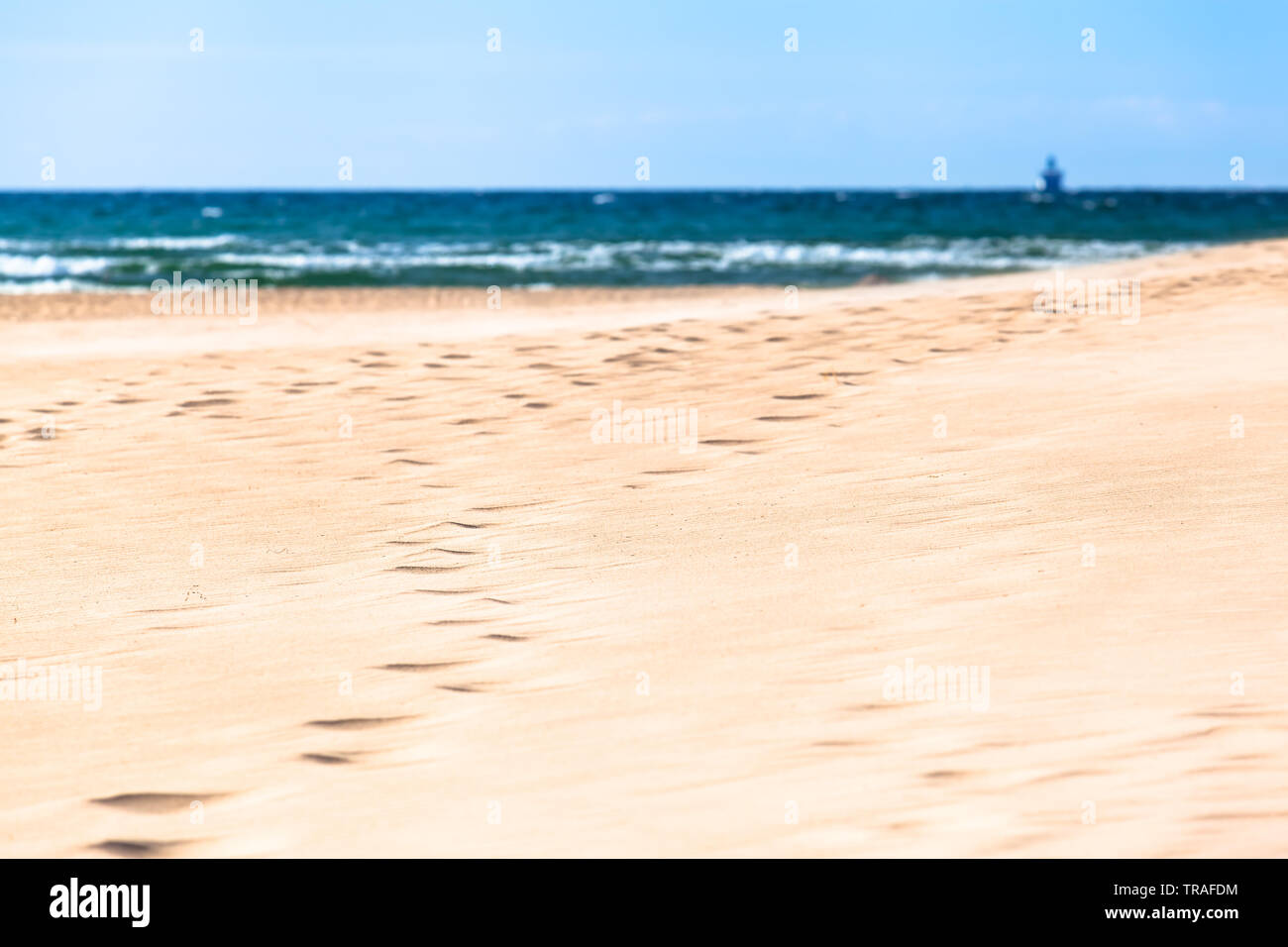 Footprints at white wide dune sand toward shore of sea,  view to small silhouette of far away ship at background horizon (copy space) Stock Photo