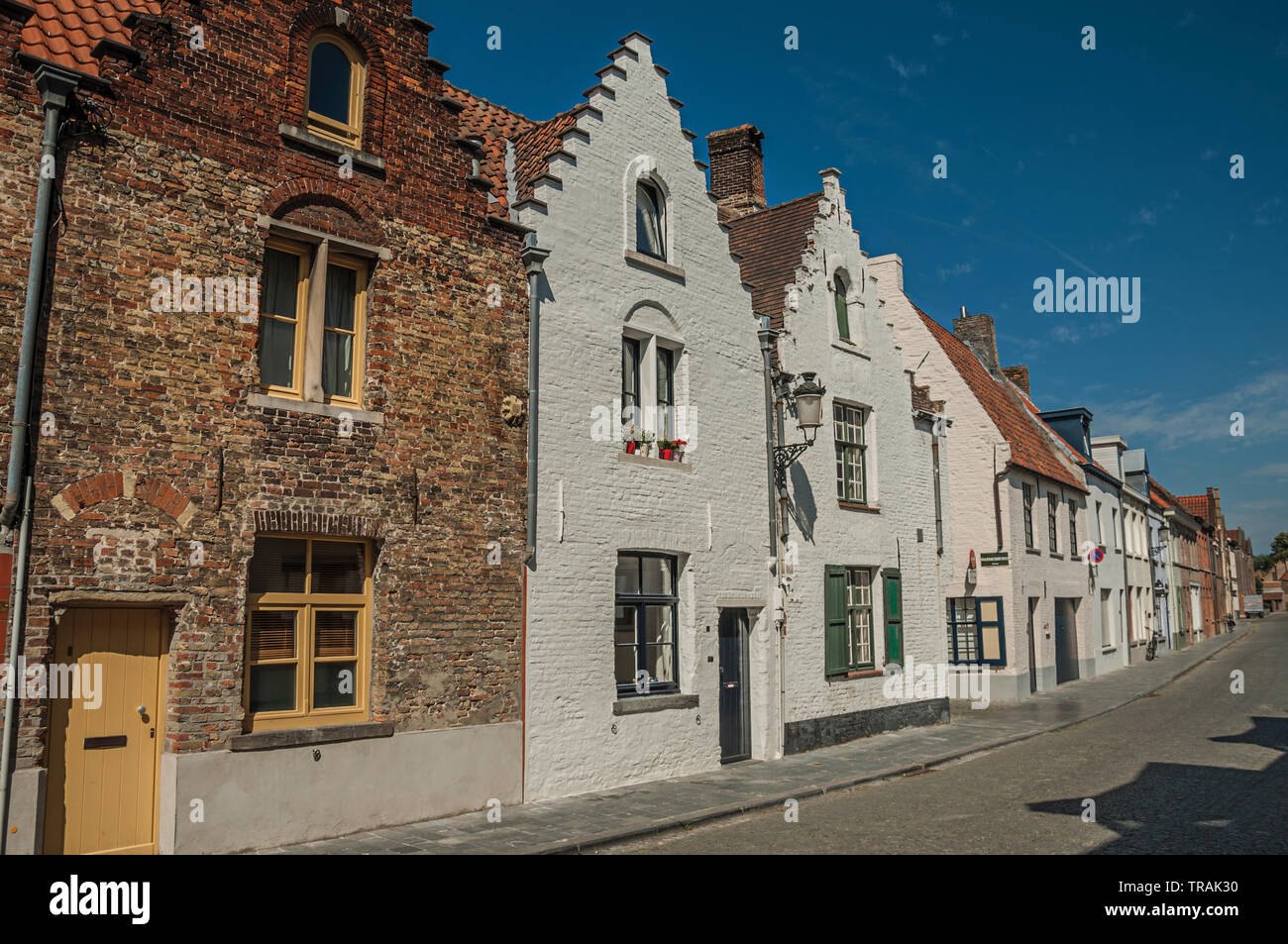 Brick facade of old houses with a blue sky in an empty street of Bruges. Charming town with canals and old buildings in Belgium. Stock Photo