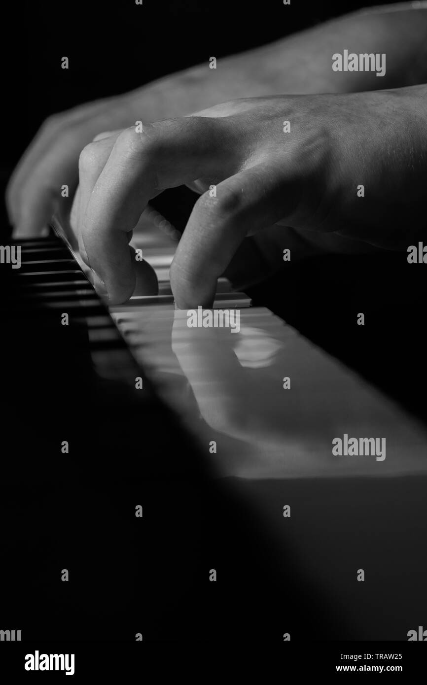 A young pianist practices in this black and white photograph with isolated hands on a piano keyboard Stock Photo