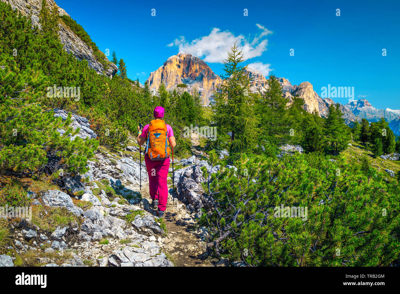 Cheerful healthy active woman hiker with colorful backpack and mountain equipment walking on the mountain path, Dolomites, Italy, Europe Stock Photo