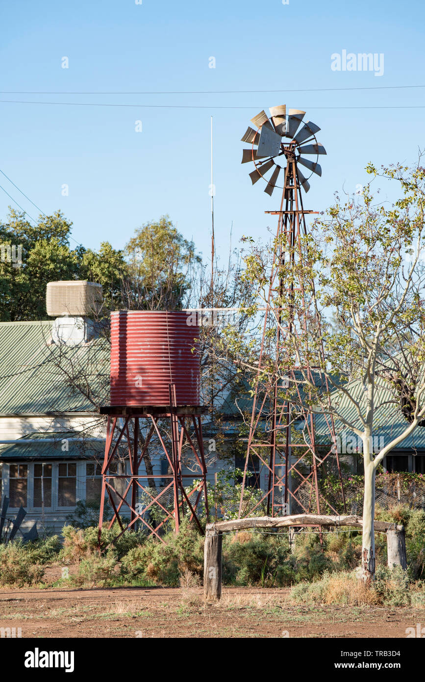 Morning sun on an old water tank, windmill and farmhouse in northwest NSW, Australia. In the foreground is an old hitching rail for resting horses Stock Photo