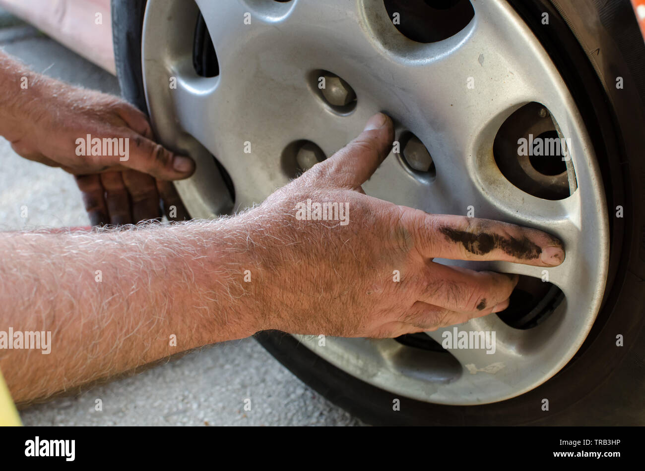 Mechanic with dirty hands replacing the plastic wheel cover after fixing tires, extreme close up