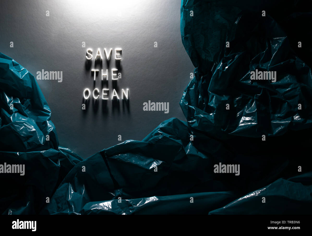 Text 'SAVE THE OCEAN' on white background lightened from above, among blue plastic bags representing ocean.Creative concept of ocean plastic pollution Stock Photo