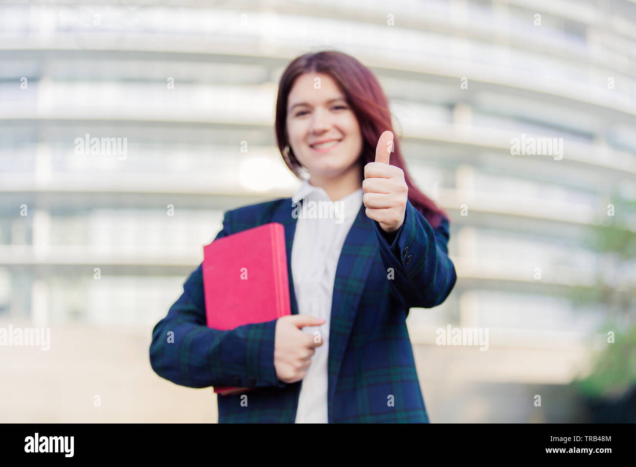 Smiling portrait of female university student with thumb up outdoors in ...