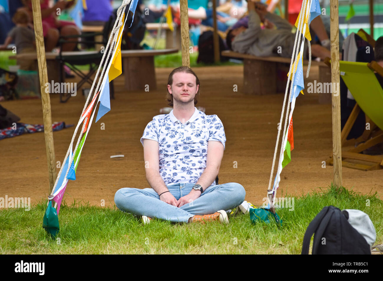 Visitor sitting cross legged relaxing outside marquee at Hay Festival Hay on Wye Powys Wales UK Stock Photo