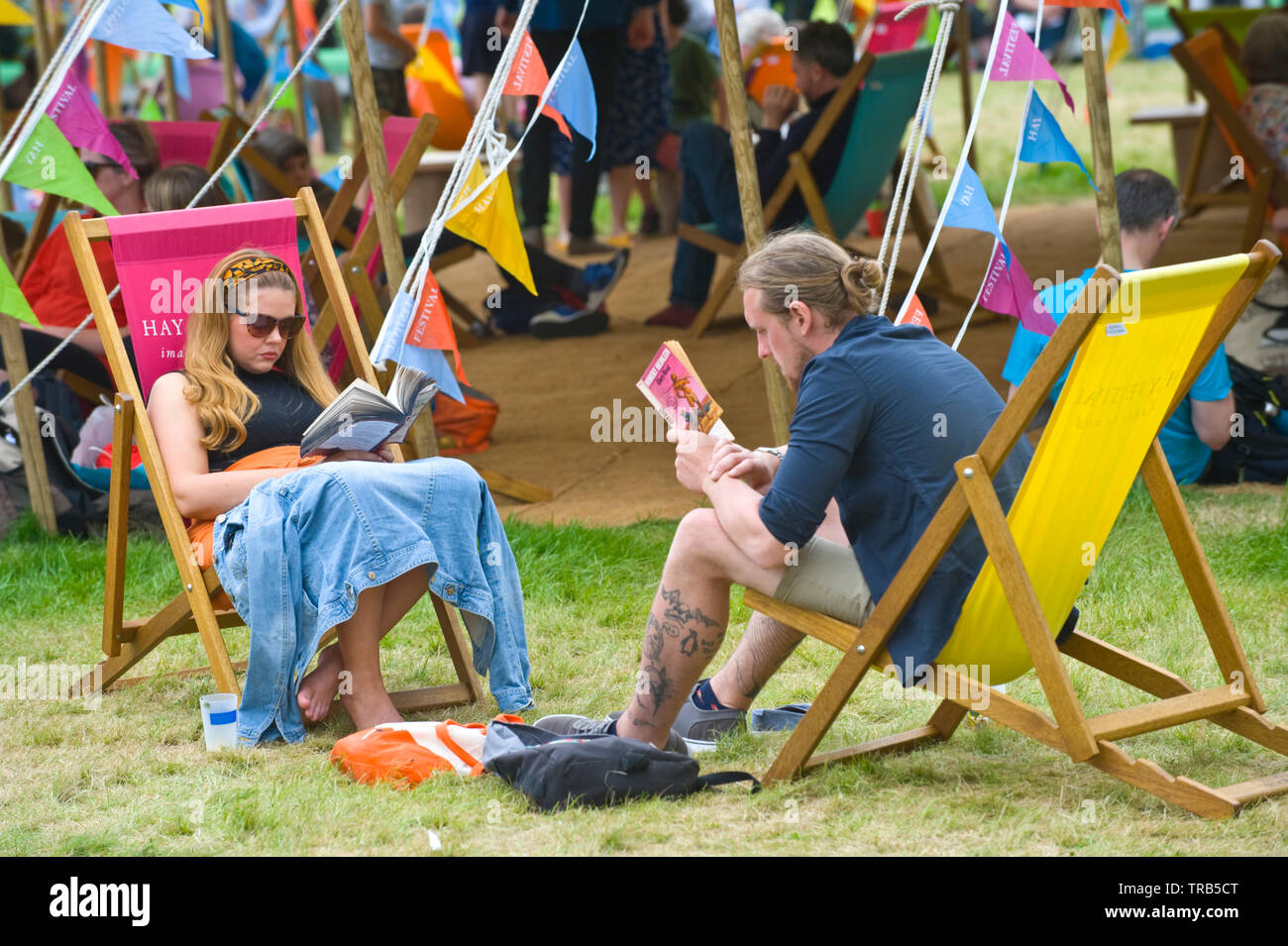 Woman and man reading books sitting in deckchairs relaxing on the lawn at Hay Festival Hay on Wye Powys Wales UK Stock Photo