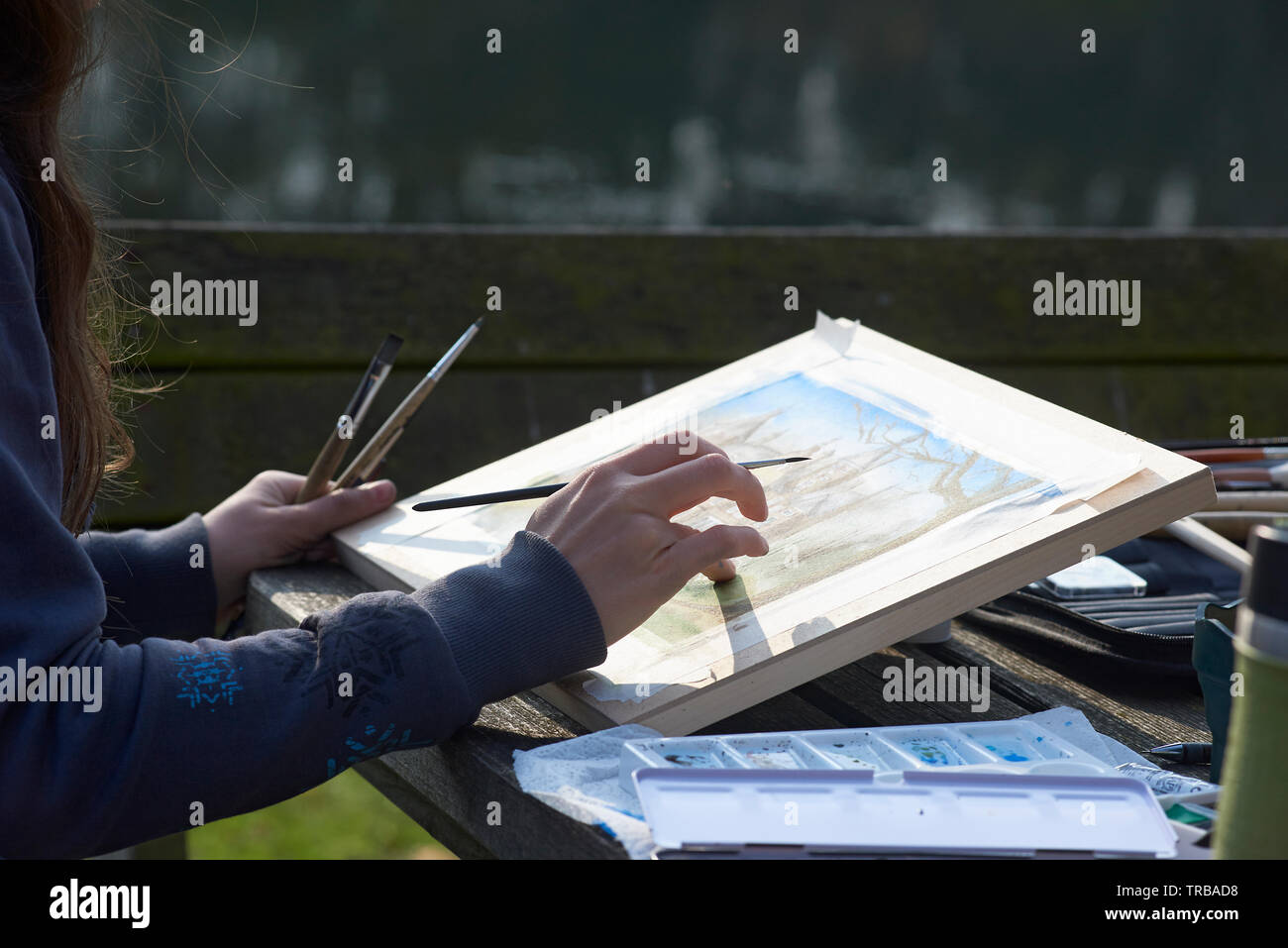 Young creative female artist sitting on a bench in a park painting a ...