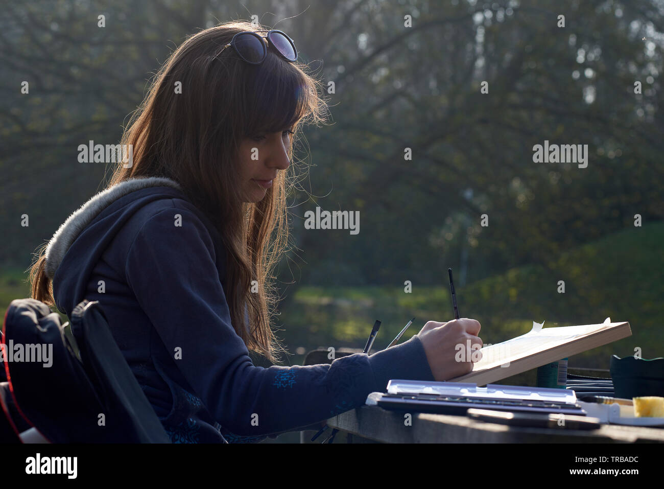 Young creative female artist sitting on a bench in a park painting a ...