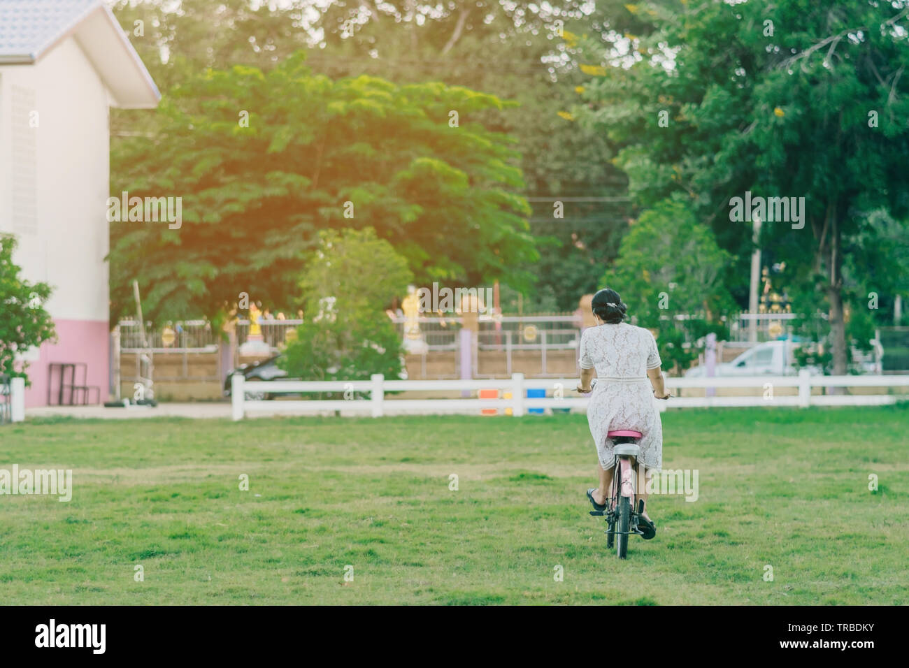 Back view of female teacher rides bicycle to teach students at ...
