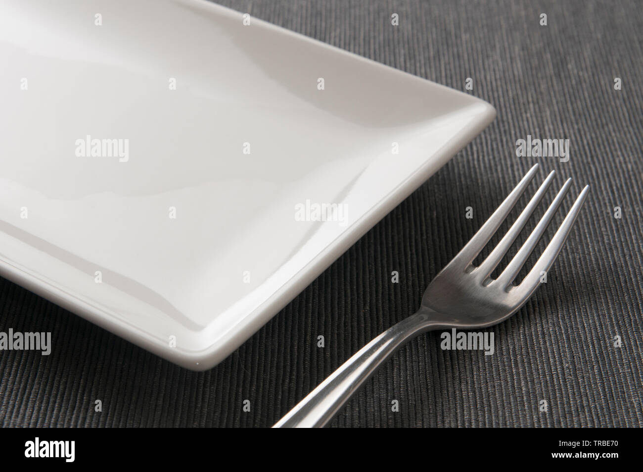 Square ceramic plate and a fork on a table Stock Photo