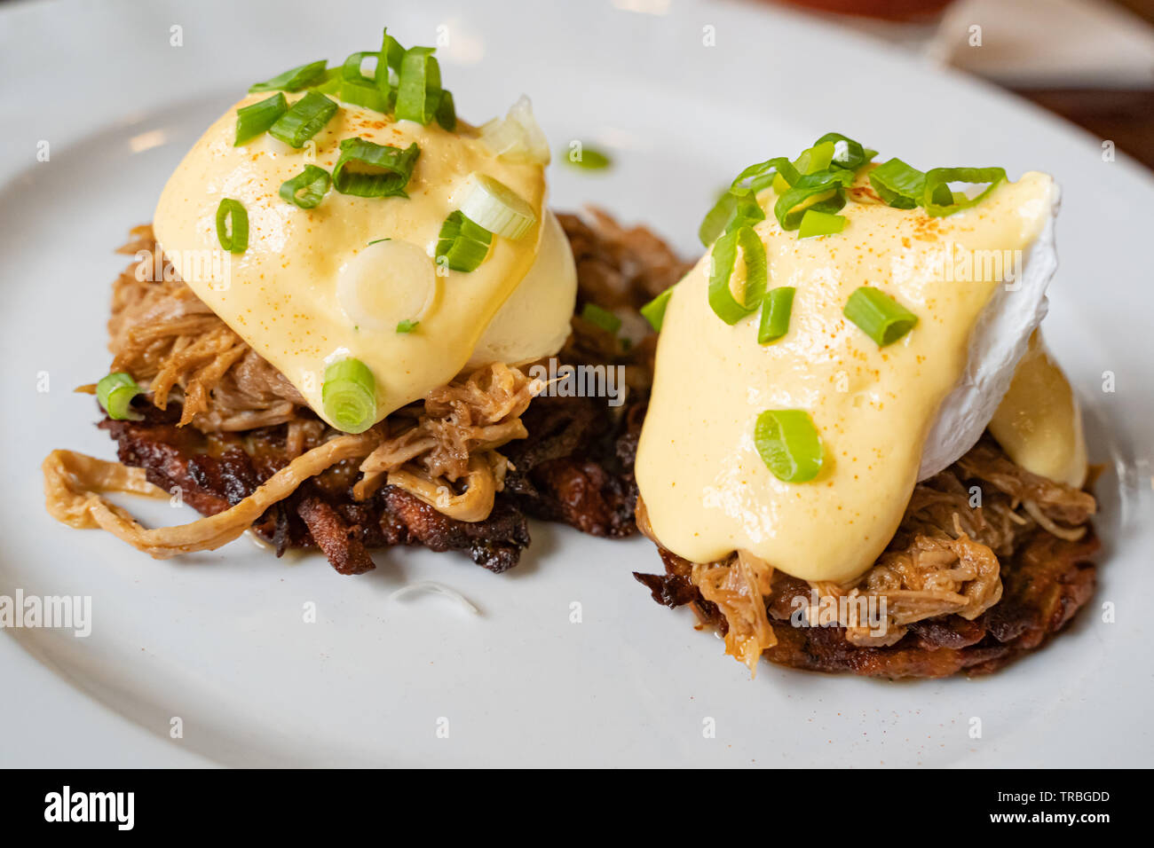 Pulled pork served on fried potato pancakes topped with poached egg and garnished with hollandaise sauce and fresh green onion aka "farmers Benedict" Stock Photo