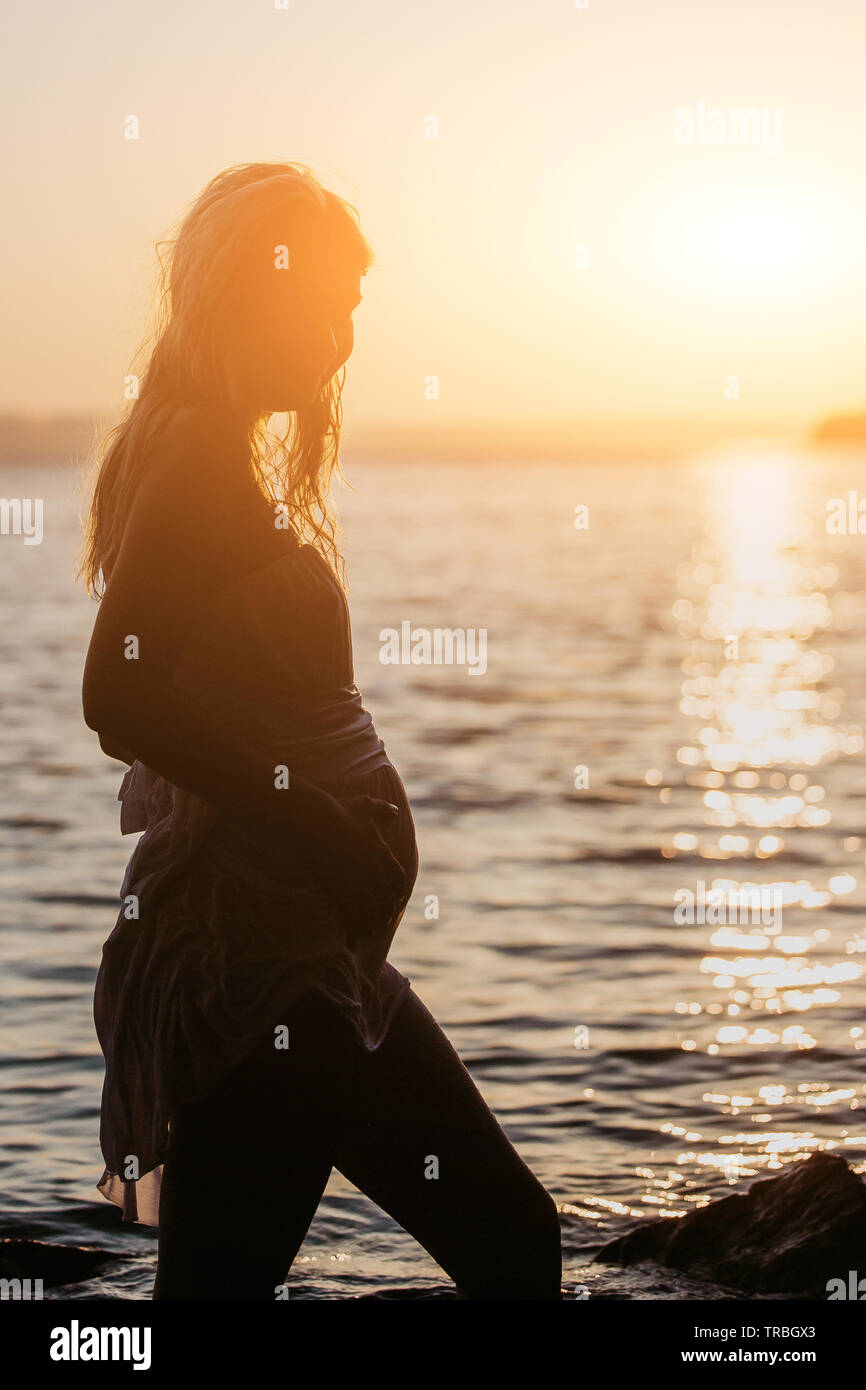 Beautiful young pregnant woman with white wet dress relax on the rocks