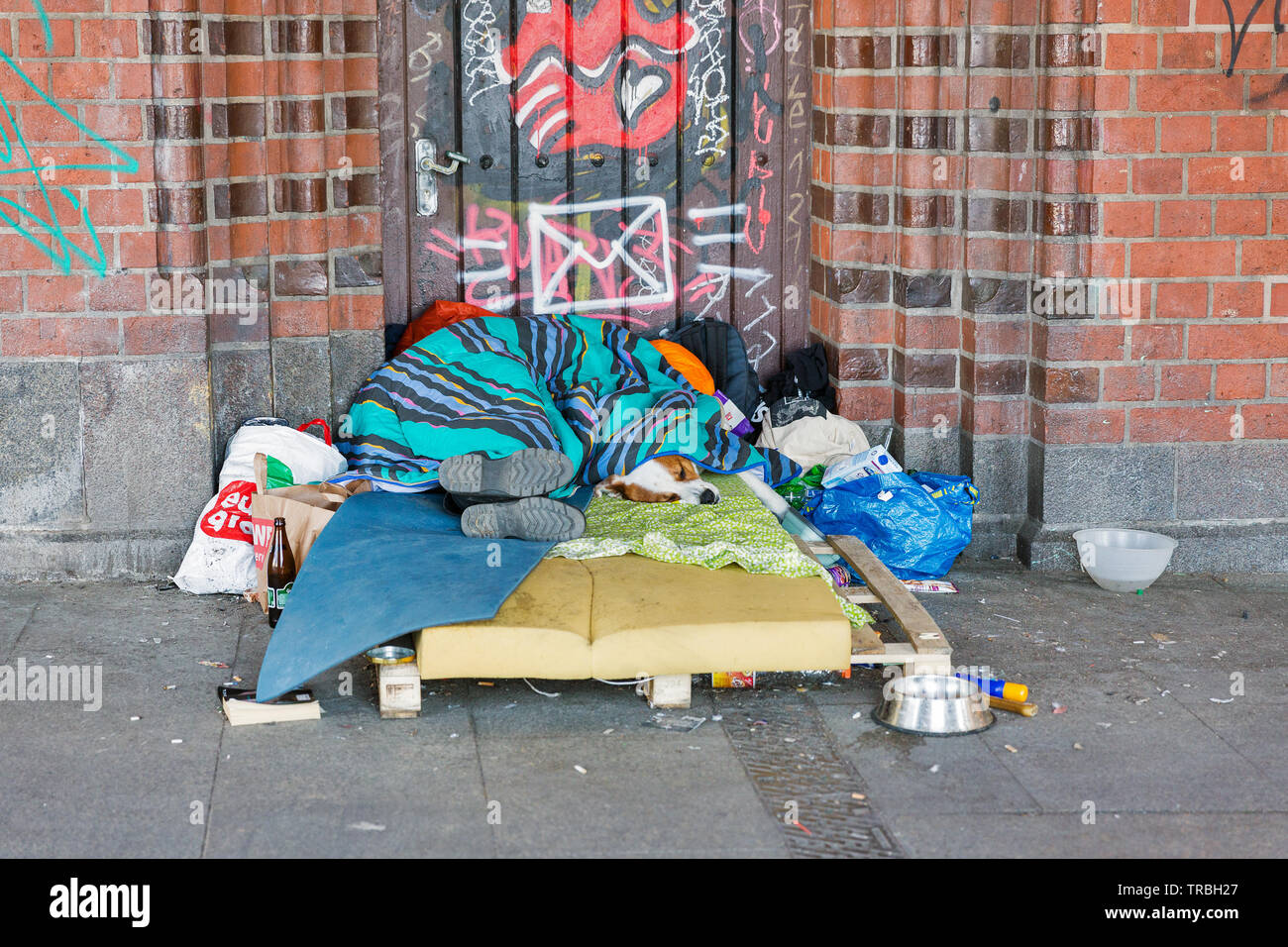 BERLIN, GERMANY - APRIL 18, 2019: A homeless man asleep over a blanketon with the dog on the ground in a Oberbaum bridge. Berlin is the capital and la Stock Photo