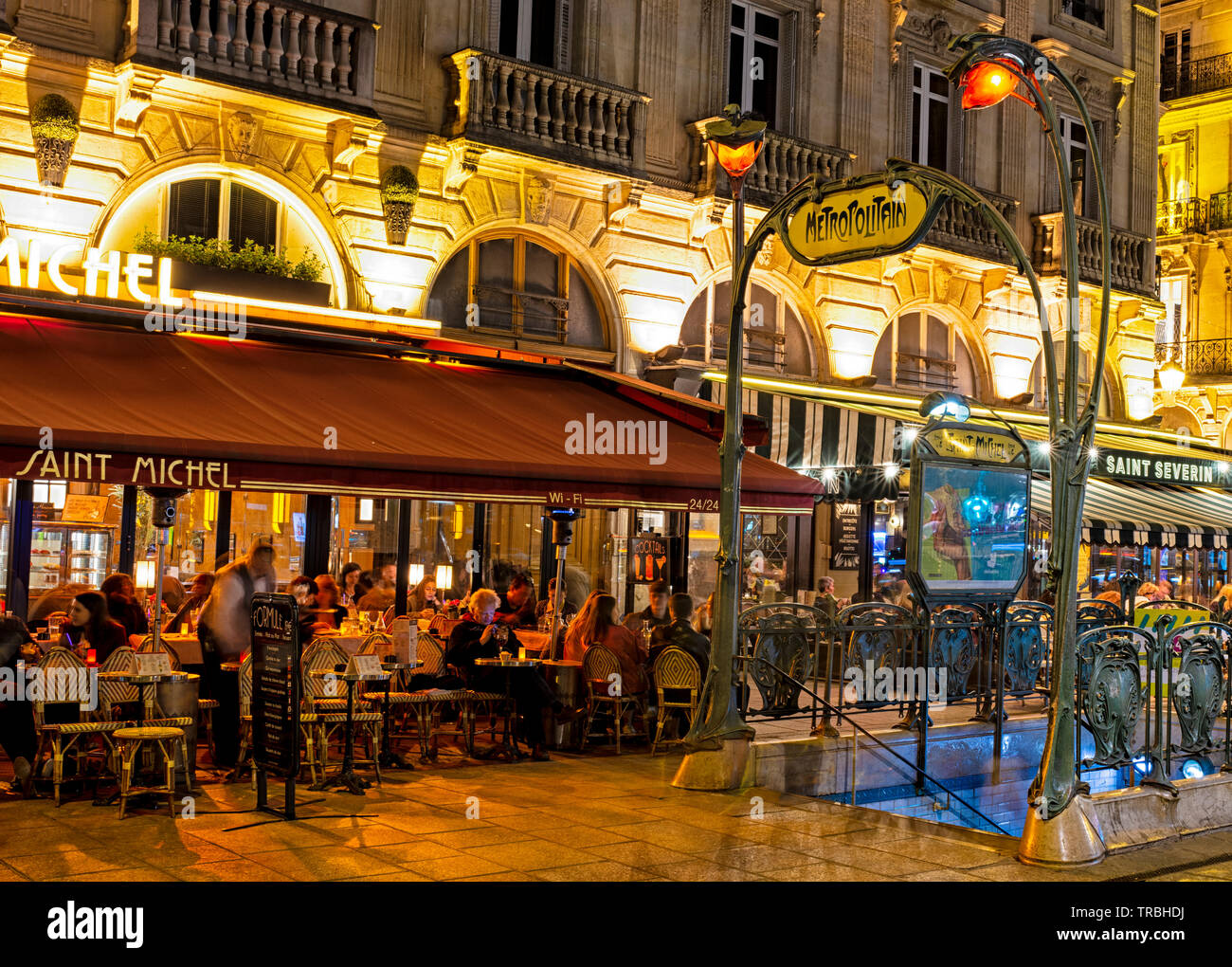 Entrance to the Metropolitain subway on Rue St. Michel in the evening with a view of restaurants and people dining outdoors. Stock Photo