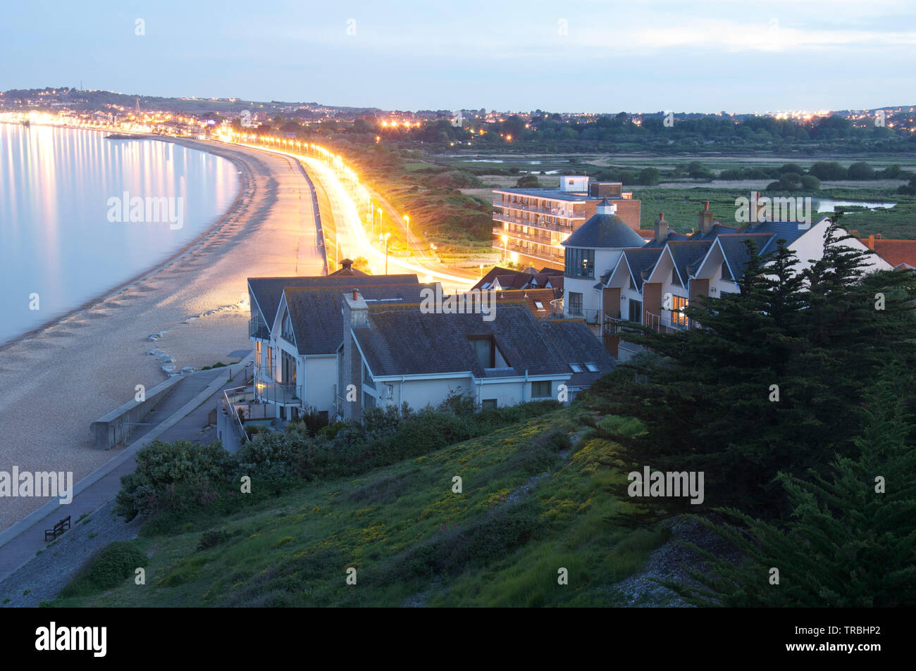 View overlooking the Dorset seaside resort of Weymouth. At dusk with street lights and car headlamps lighting up the shingle beach. South-west England. Stock Photo