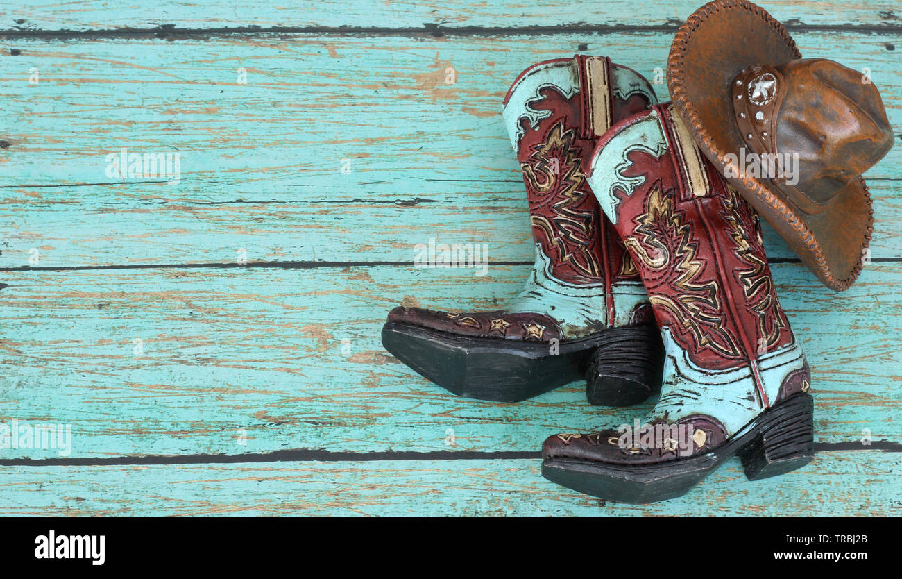 teal and burnt red cowboy boots and hat on a teal wooden background with writing space Stock Photo