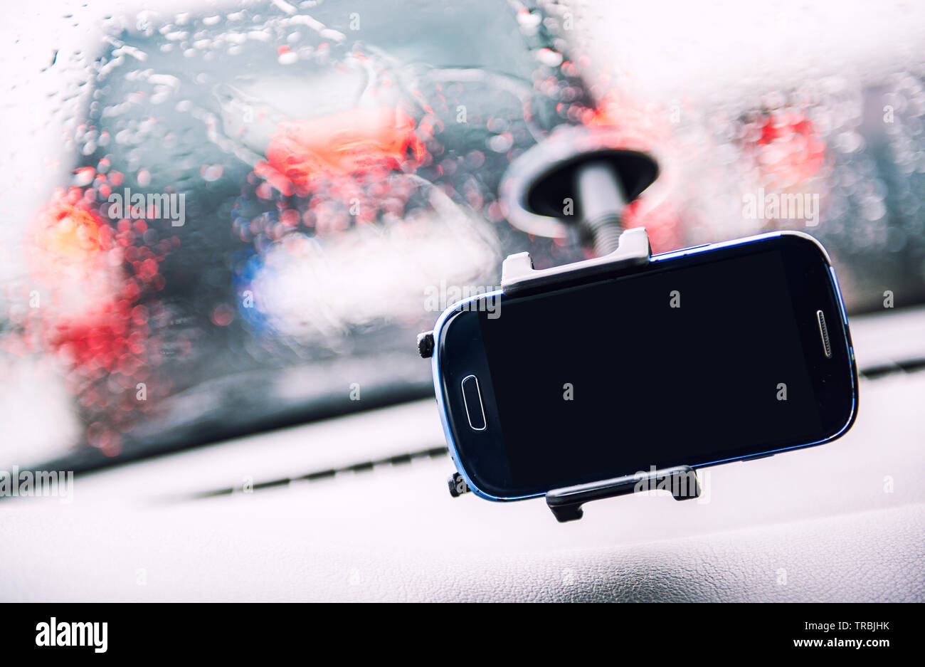 Smart phone on holder, rainy weather seen through wind shield, cellphone with black mock up blank on screen. Advertisement for traffic and navigation Stock Photo