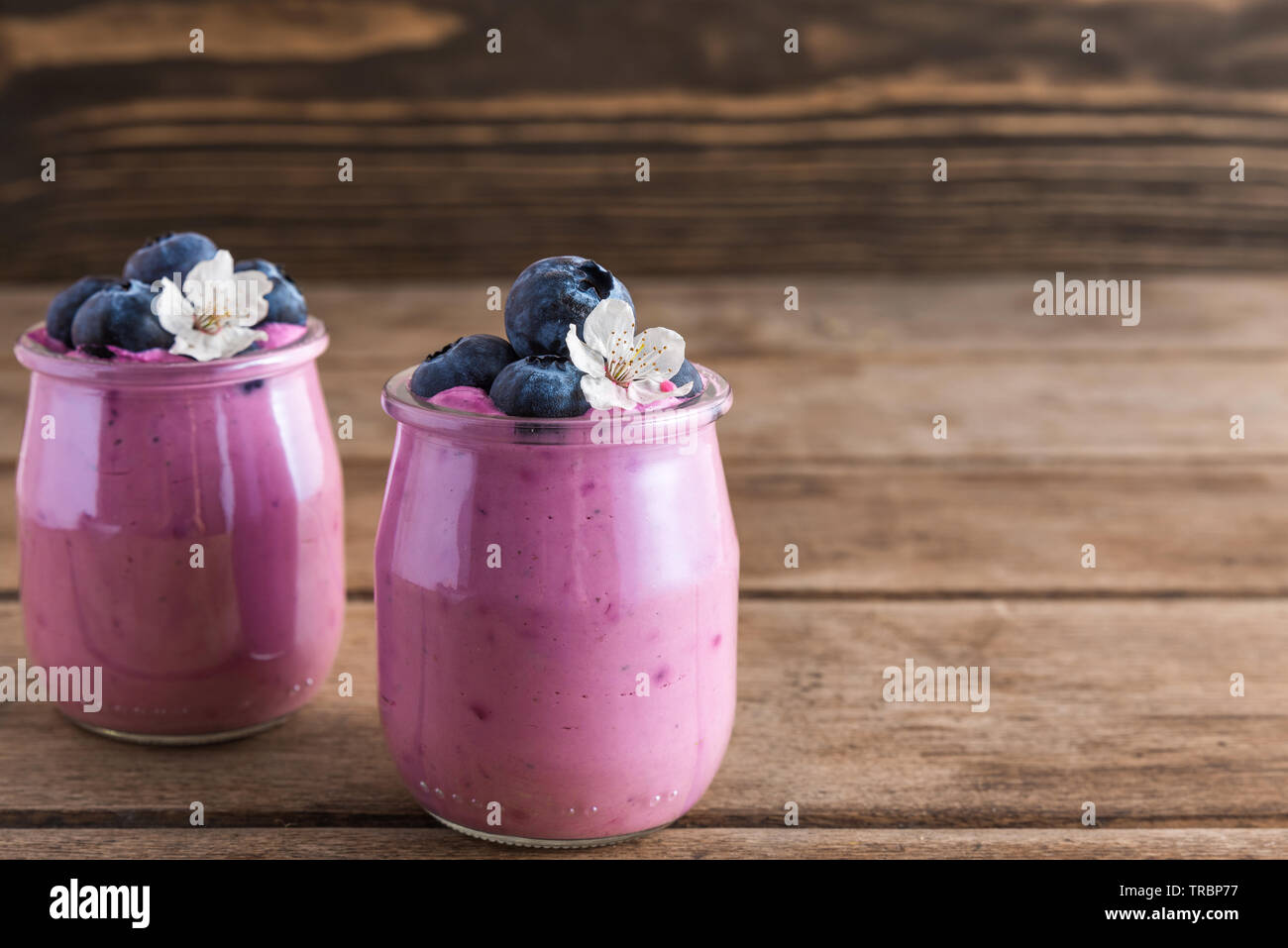 Two glasses of blueberry yogurt with fresh blueberries and spring flowers for healthy breakfast on rustic wooden background. close up Stock Photo