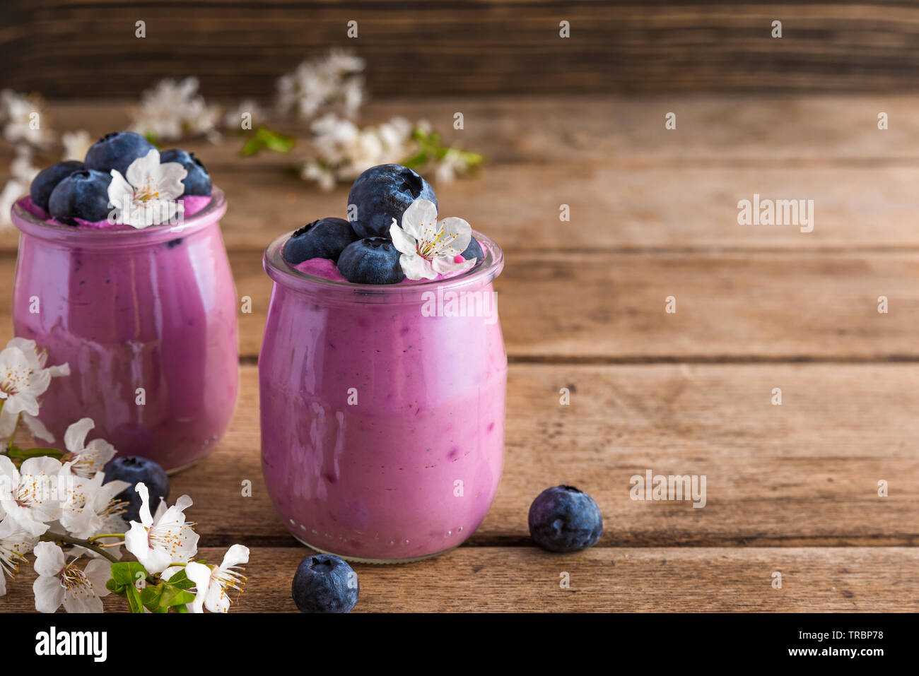 healthy breakfast. Blueberry yogurt in glasses served with fresh blueberries and spring blossom cherry flowers on rustic wooden table. close up Stock Photo