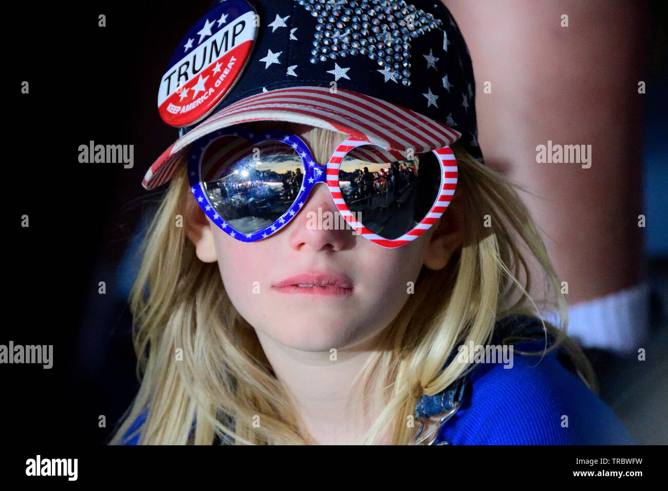A young supporter in patriotic hat and glasses bites her lip while watching  US President Donald J. Trump boarding a Boeing C-32, Air Force One Stock Photo