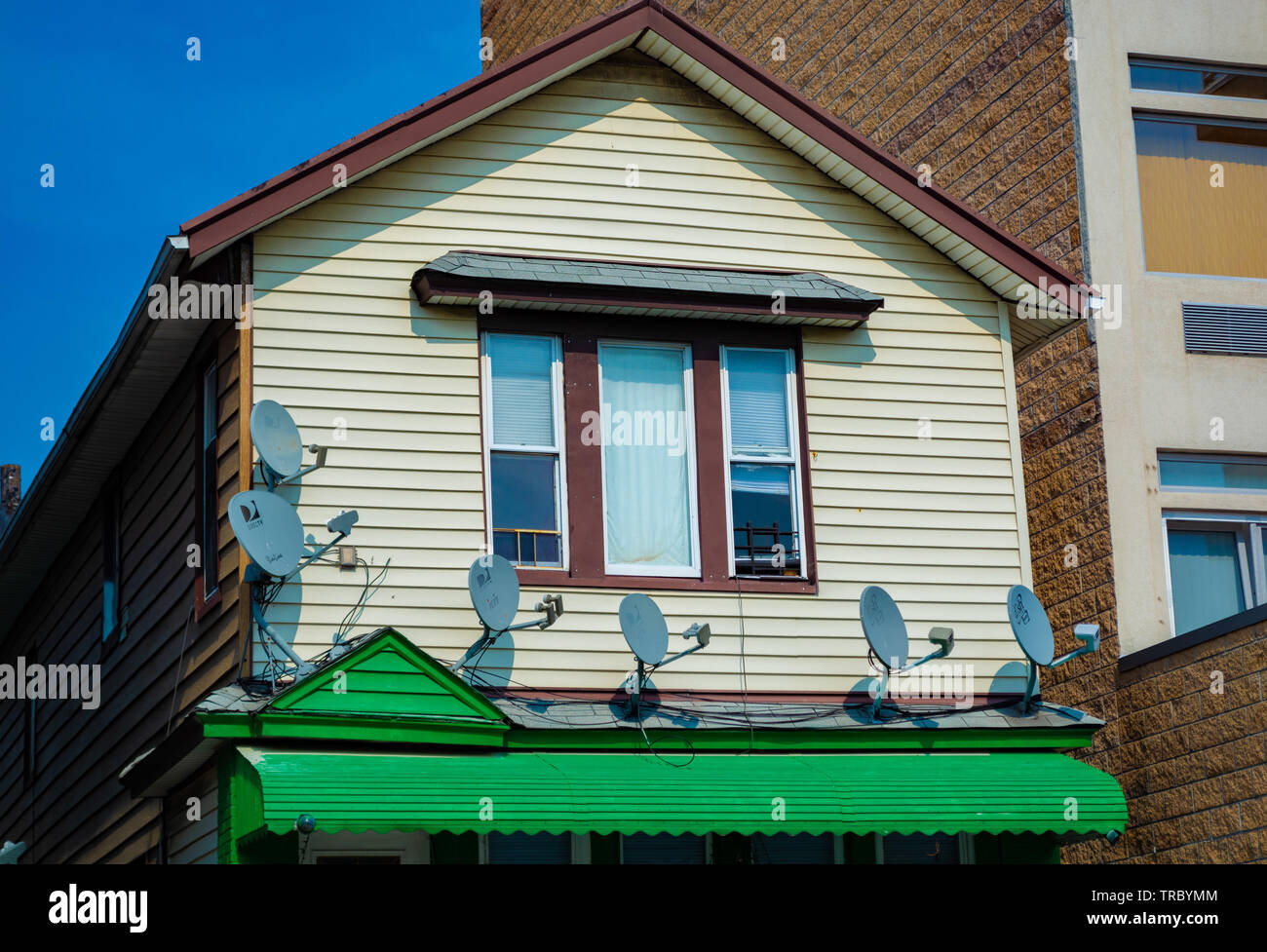 A two family house with 6 direct tv satellite antennas attached to it and sunny blue sky day. Stock Photo
