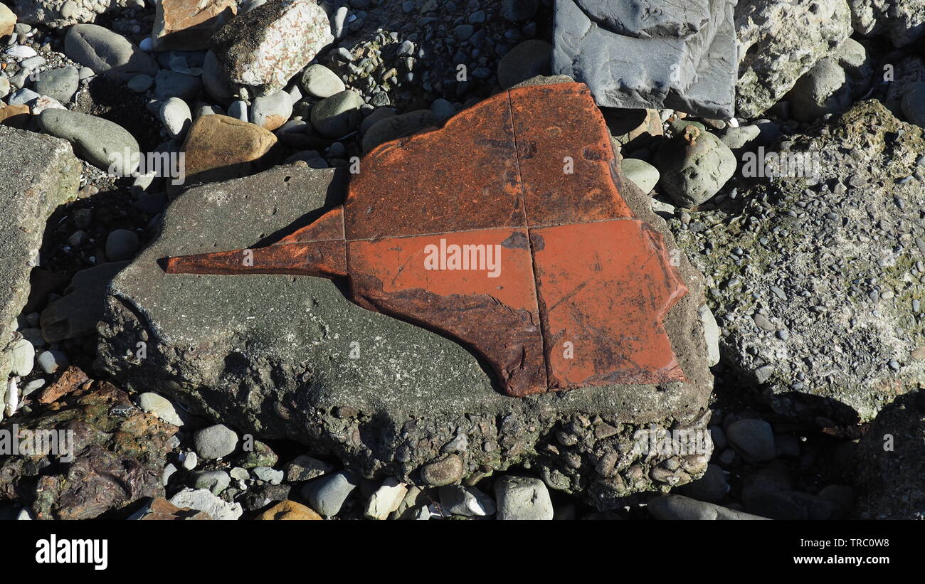 In this fund art object, thin red terracotta tiles, still glued to concrete and broken in curved edges, resembles an angel fish beached on foreshore Stock Photo