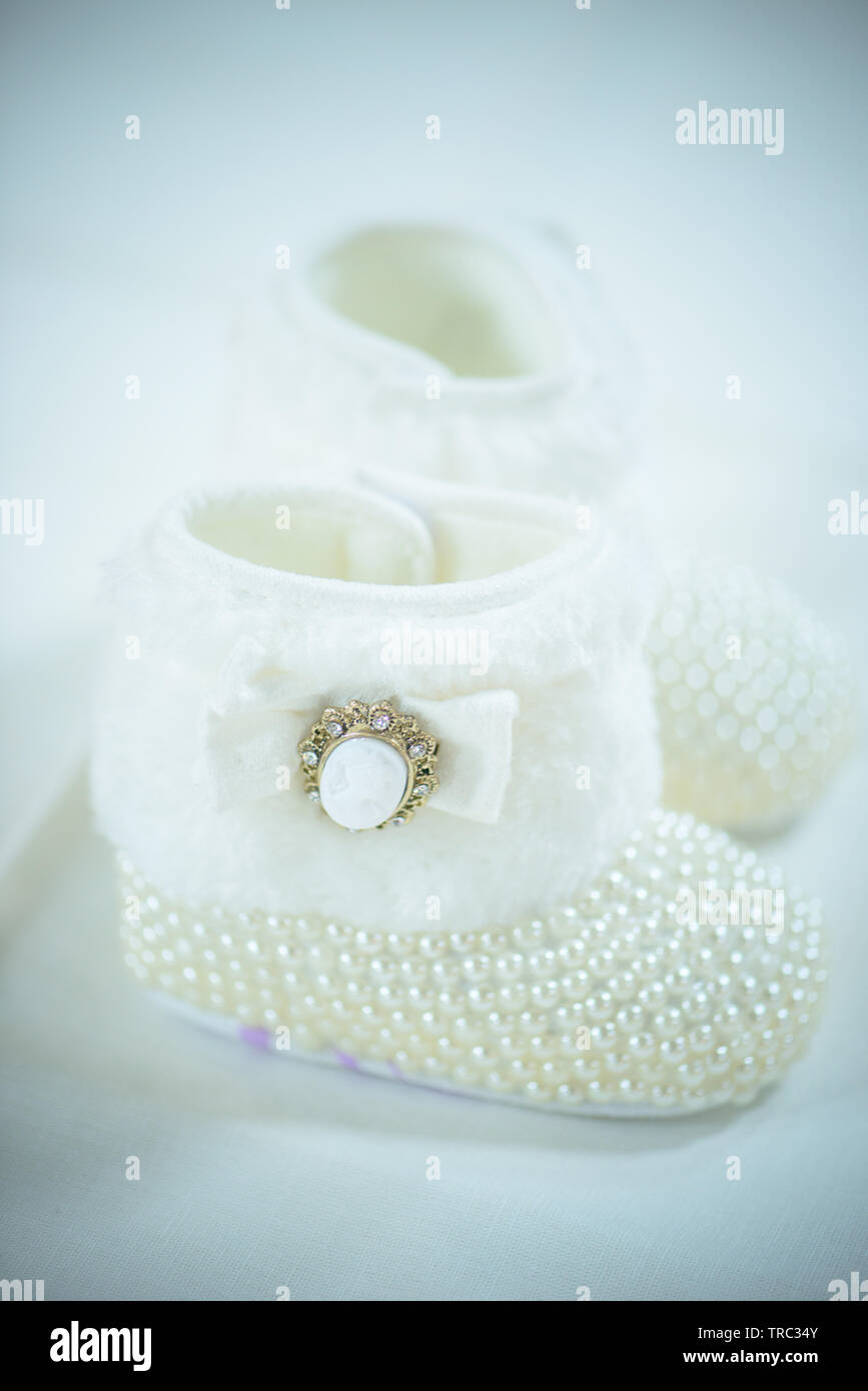 Elegant white wool booties with vintage cameo brooch decoration element and pearls-like beads covered vamp, adorable footwear for baby girls Stock Photo