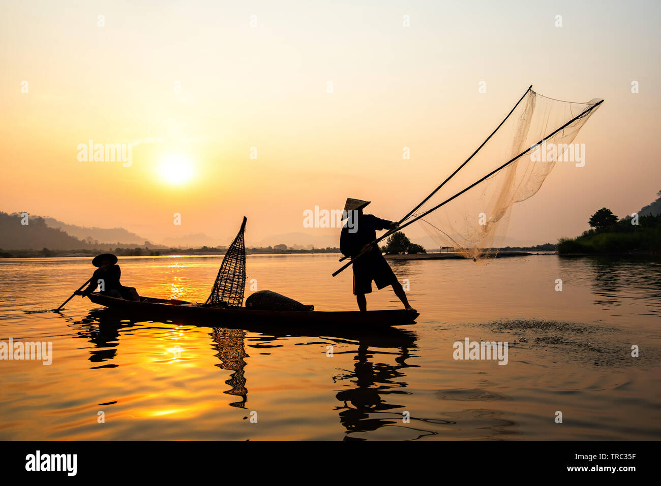 Asia fisherman net using on wooden boat casting net sunset or sunrise in  the Mekong river - Silhouette fisherman boat with mountain background life  pe Stock Photo - Alamy