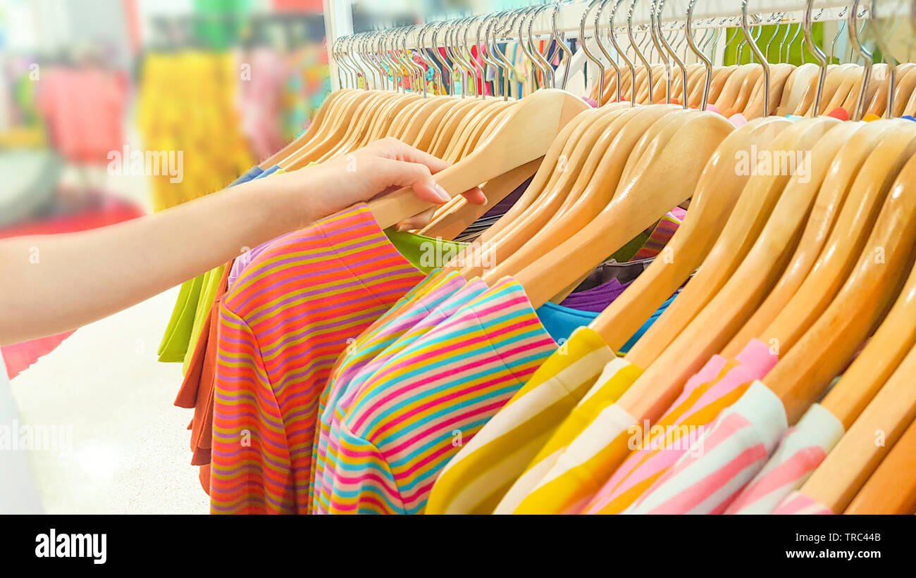 Buying Clothes in A Shopping Mall Store. Close Up of Woman Hand Choosing and Discount Colorful T-Shirt on Hanger in Store. People Standing to Finding Stock Photo