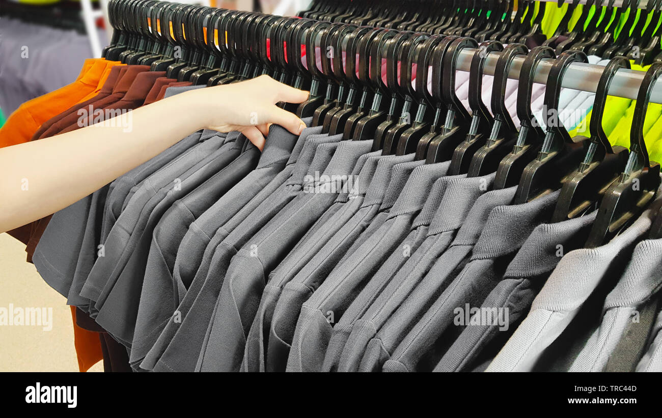 Hand of Customer Choosing Discount Clothes in a Shopping Mall. People Searching or Buying Cheap Cotton Gray T-Shirt on Rack Hanger in a Clothing Store Stock Photo