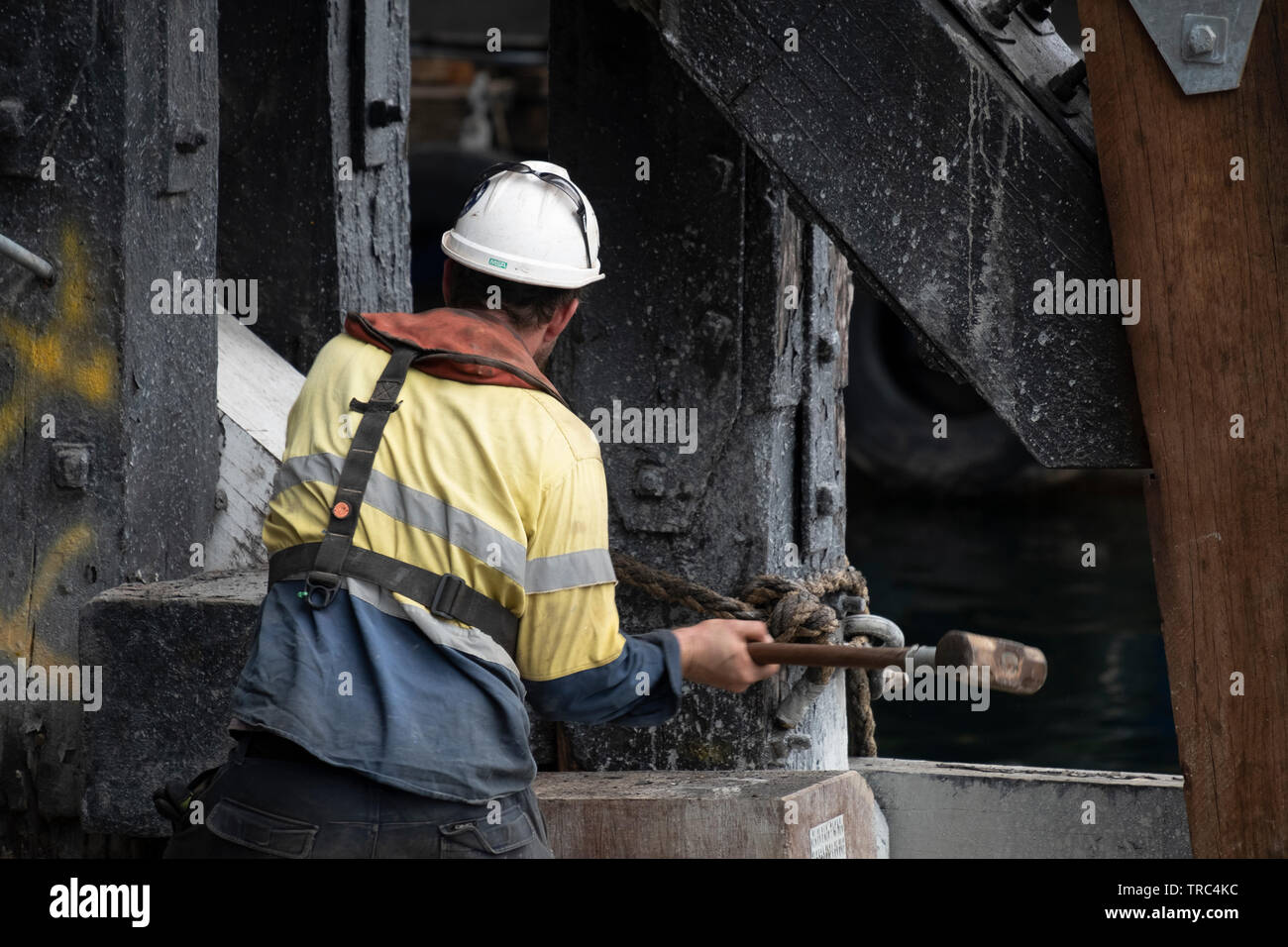 A man in a hard hat, wielding a sledgehammer, works repairing the underside of Pyrmont Bridge, Sydney, Australia. Stock Photo