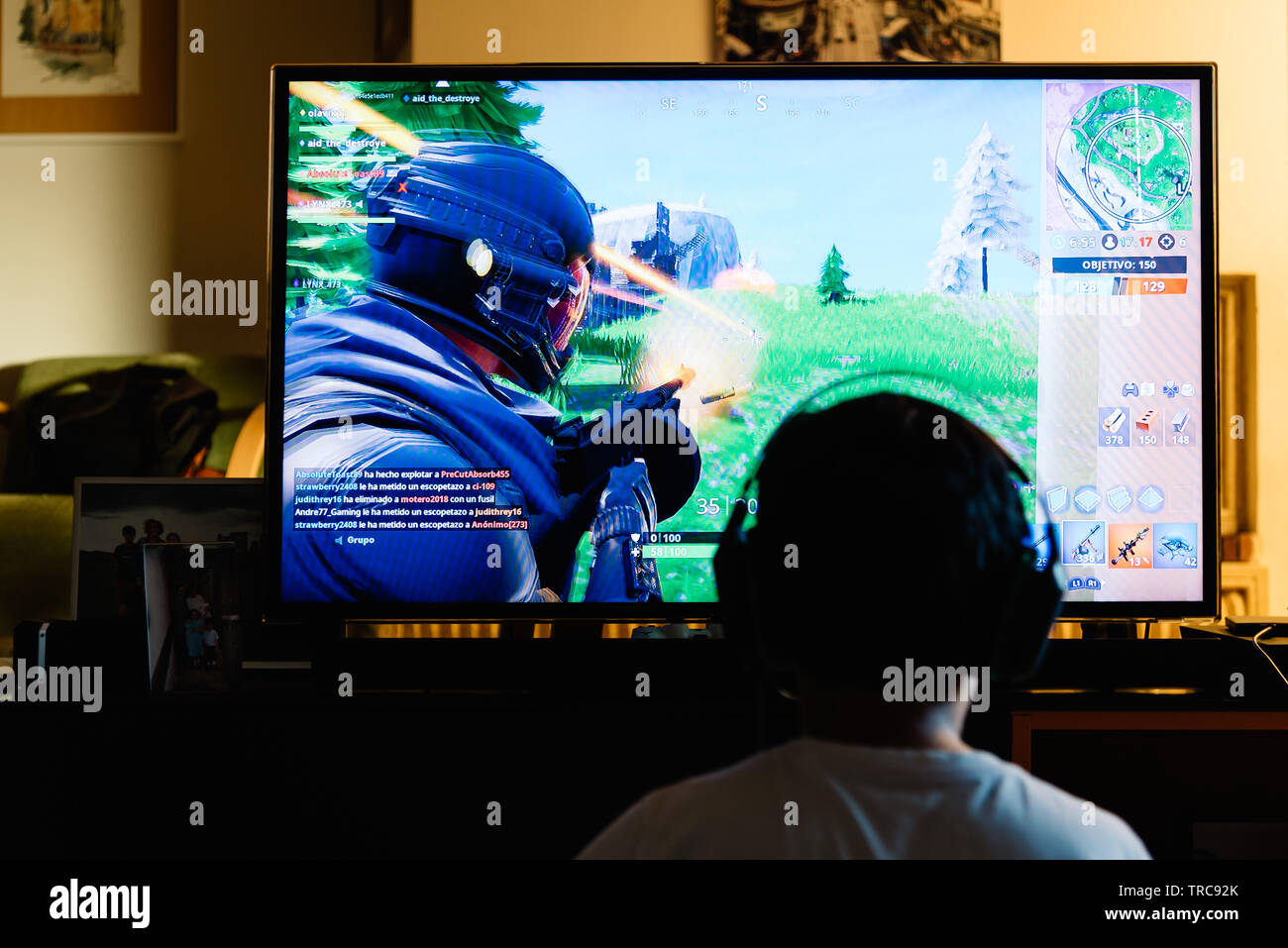 Madrid, Spain - May 29, 2019: Teenager playing Fortnite video game withn Playstation on TV. Fortnite is an online multiplayer video game developed by Stock Photo