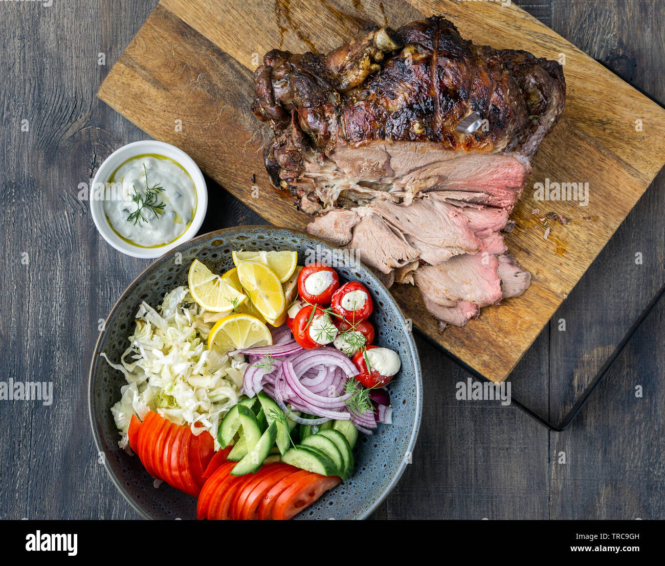 Delicious Lamb leg roast cooked on a rotisserie served with fresh greek salad and sauce for souvlaki wraps. Stock Photo