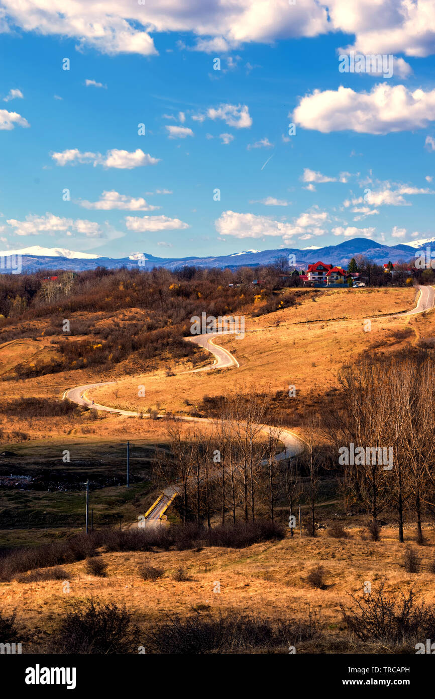 winding road thru hills in early spring time and snow covered mountain peaks in the far background Stock Photo