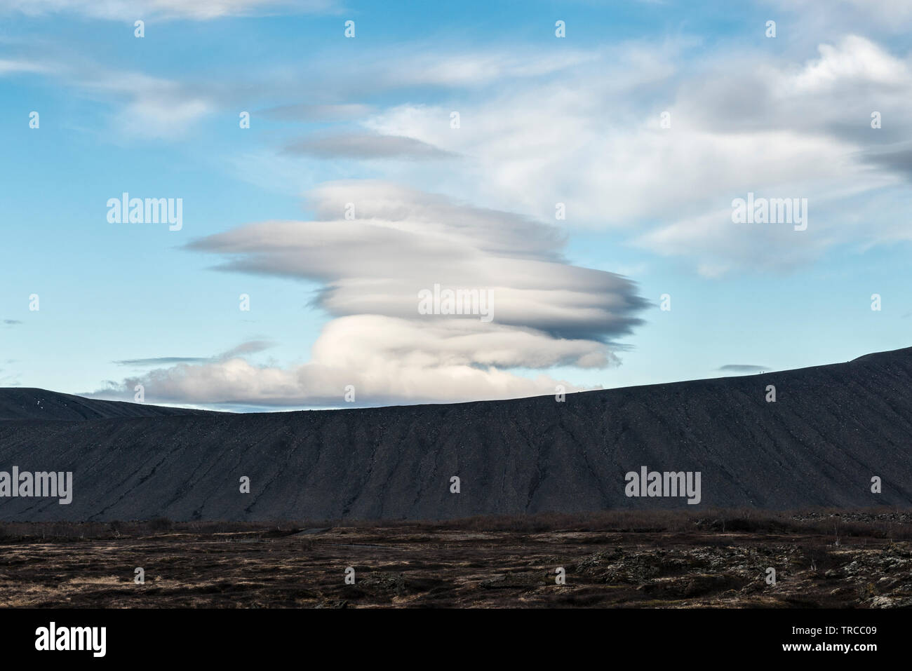 A lenticular cloud over the huge volcanic crater of Hverfjall, Lake Myvatn, Iceland. The tiny figures of two hikers can be seen (rt) on the crater rim Stock Photo