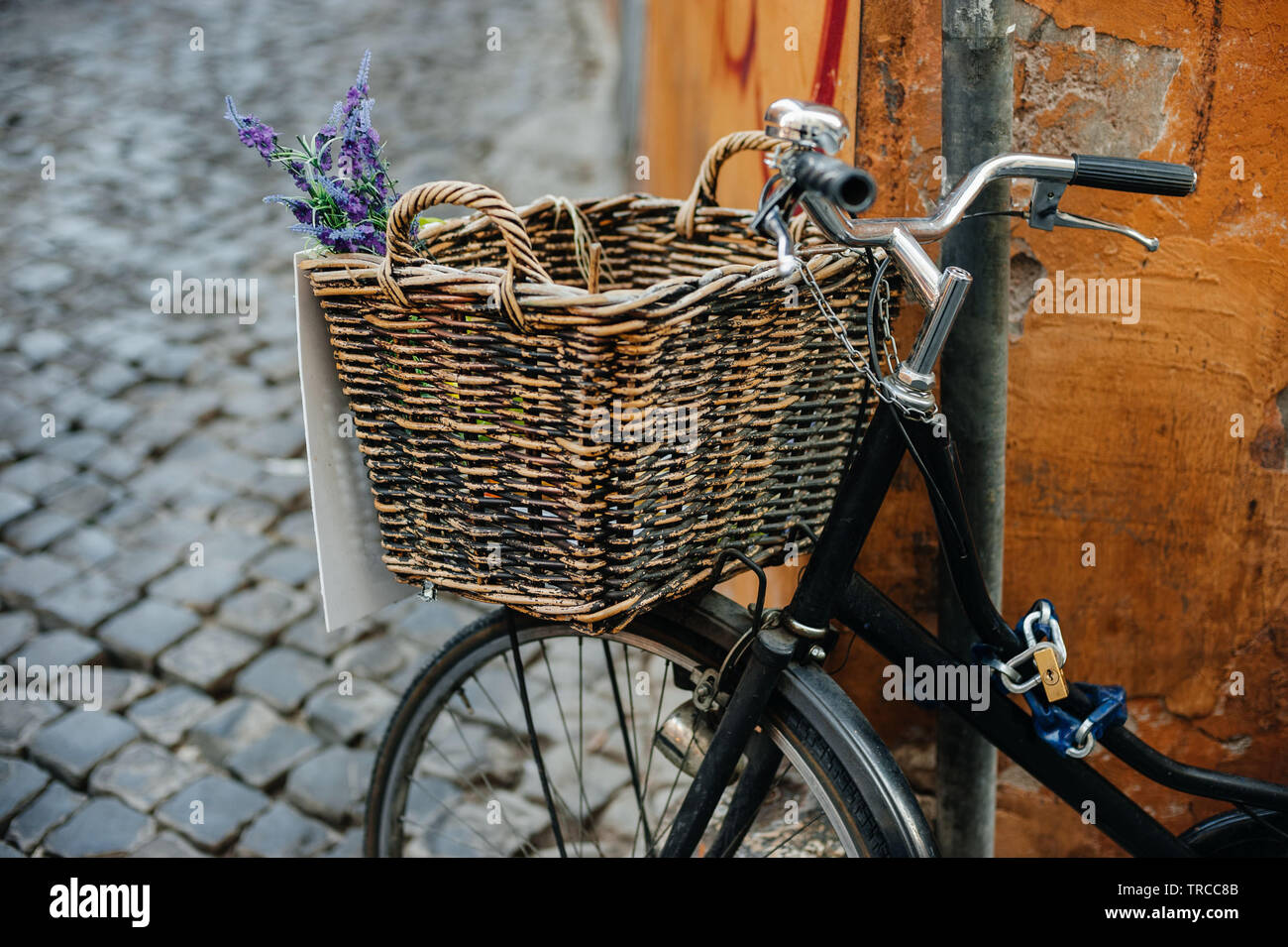 Black vintage bicycle with brown wooden basket and blue flowers on the city street near orange wall Stock Photo