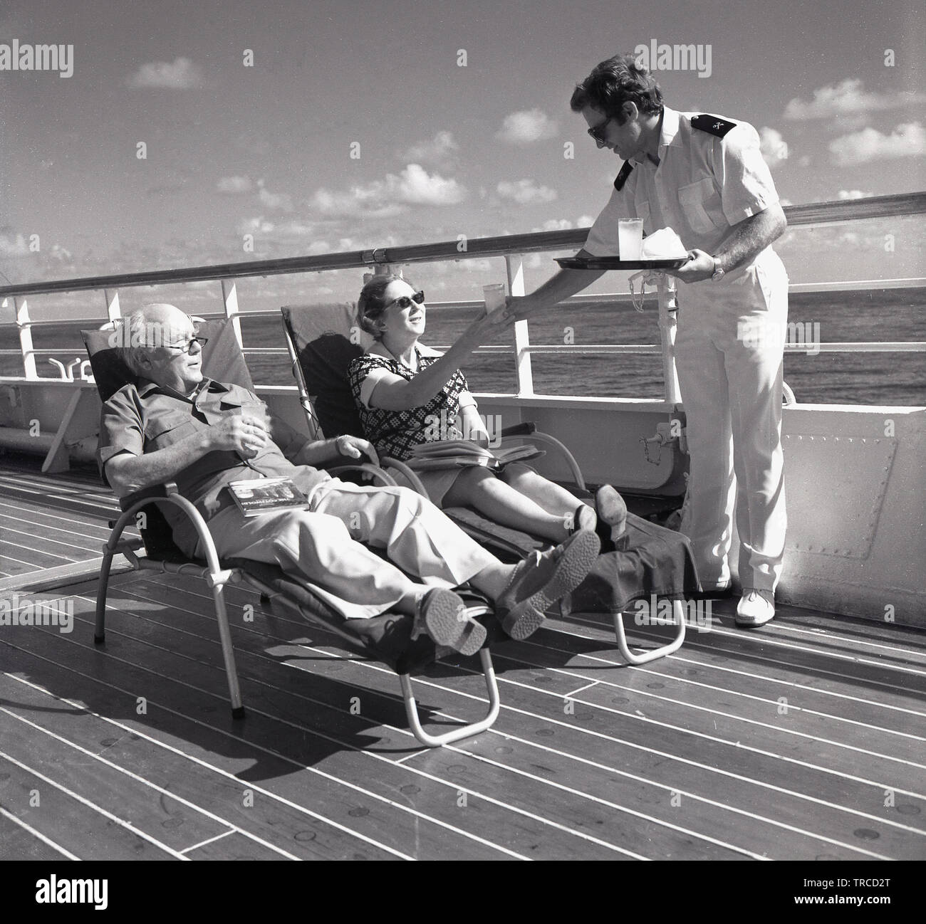 1960s Historical Two Cruise Ship Passengers Playing A Deck Game Of Shuffleboard Where Players Use Long Sticks With Curved Tips To Slide Rubber Disks Across A Court Painted Onto The Deck It